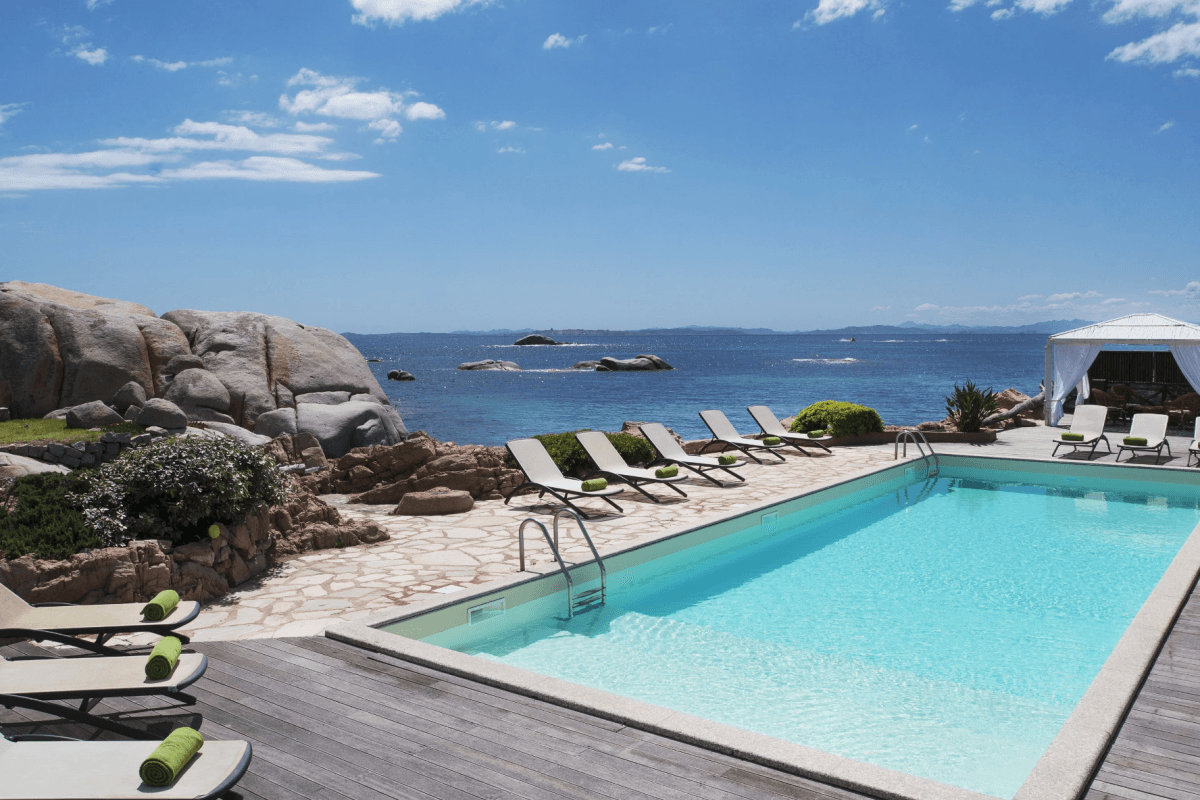 white lounge chairs surround a pool on a wooden seaside pool deck