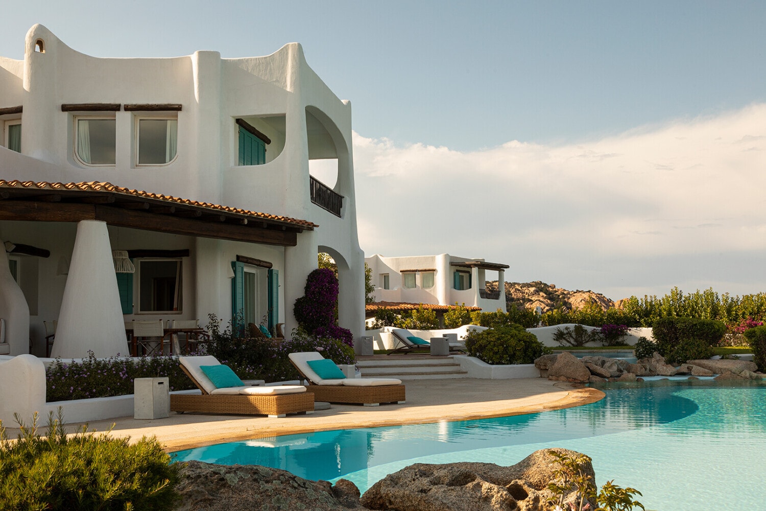 a white stucco building in front of a light-blue pool