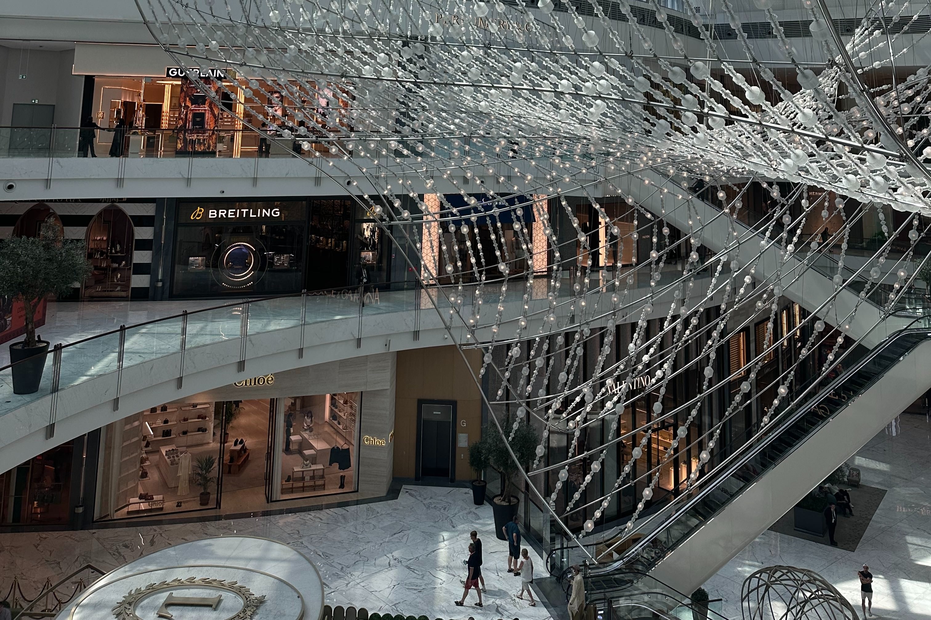 An indoor shopping center with an elaborate glass structure hanging from the ceiling over three stories of store fronts. 