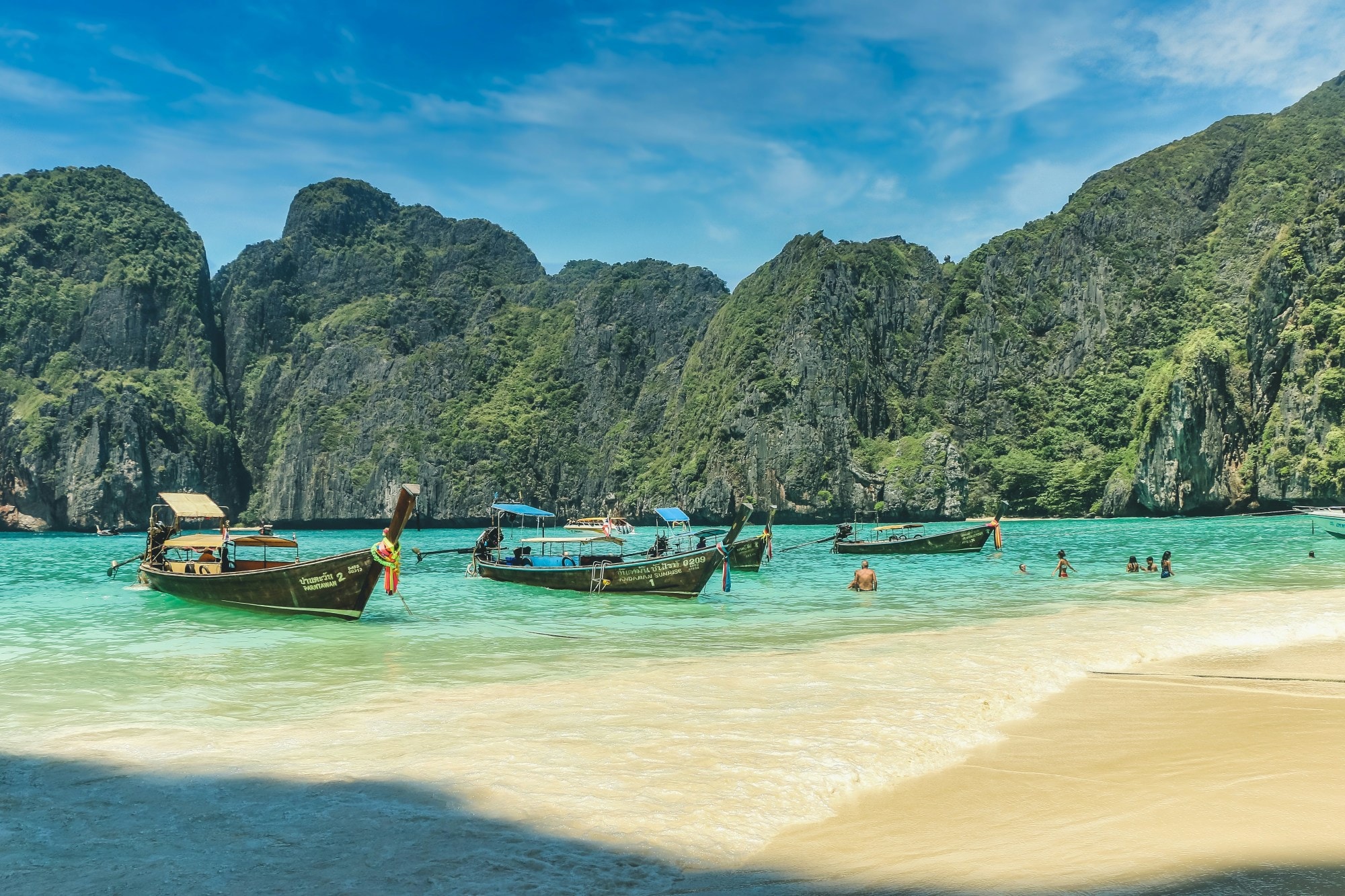 Three boats with people on a beautiful beach with green rocky hills.