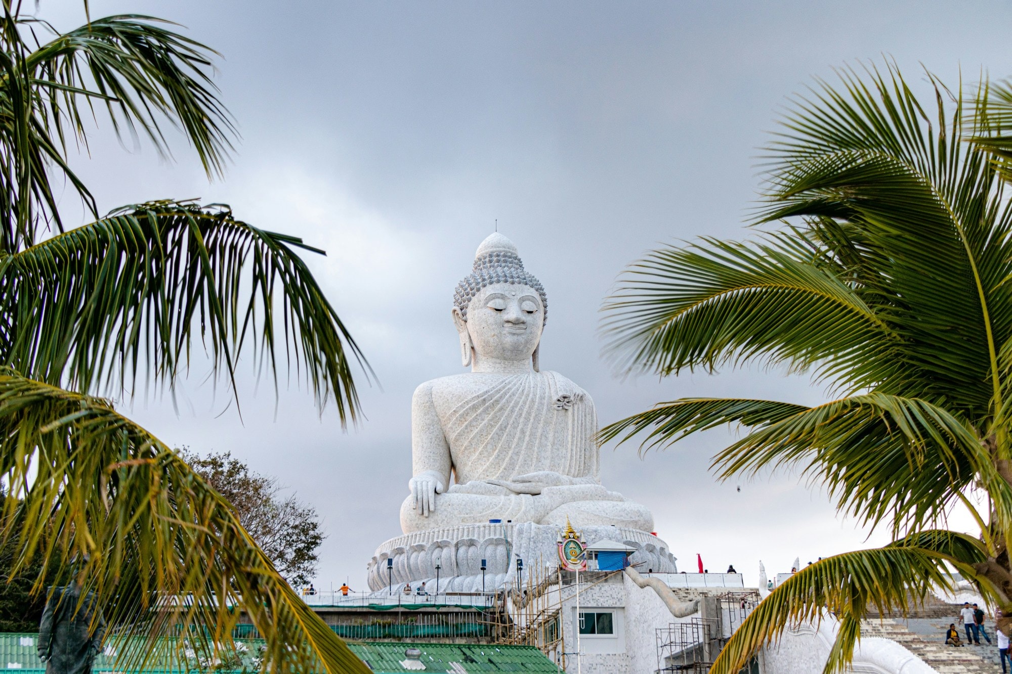 A big white Buddha statue with palm trees during daytime.