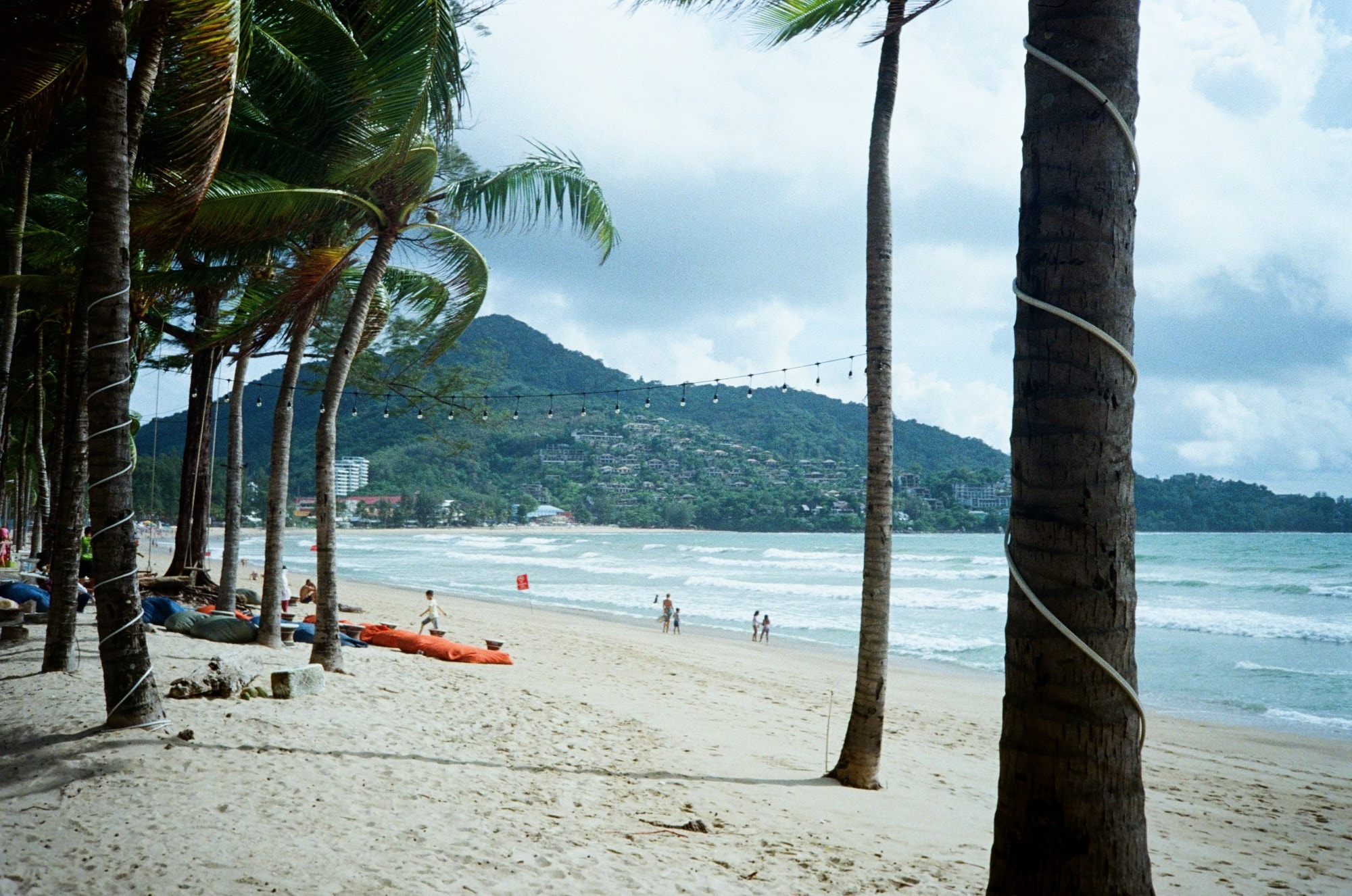 A beach with palm trees and people and mountain in view