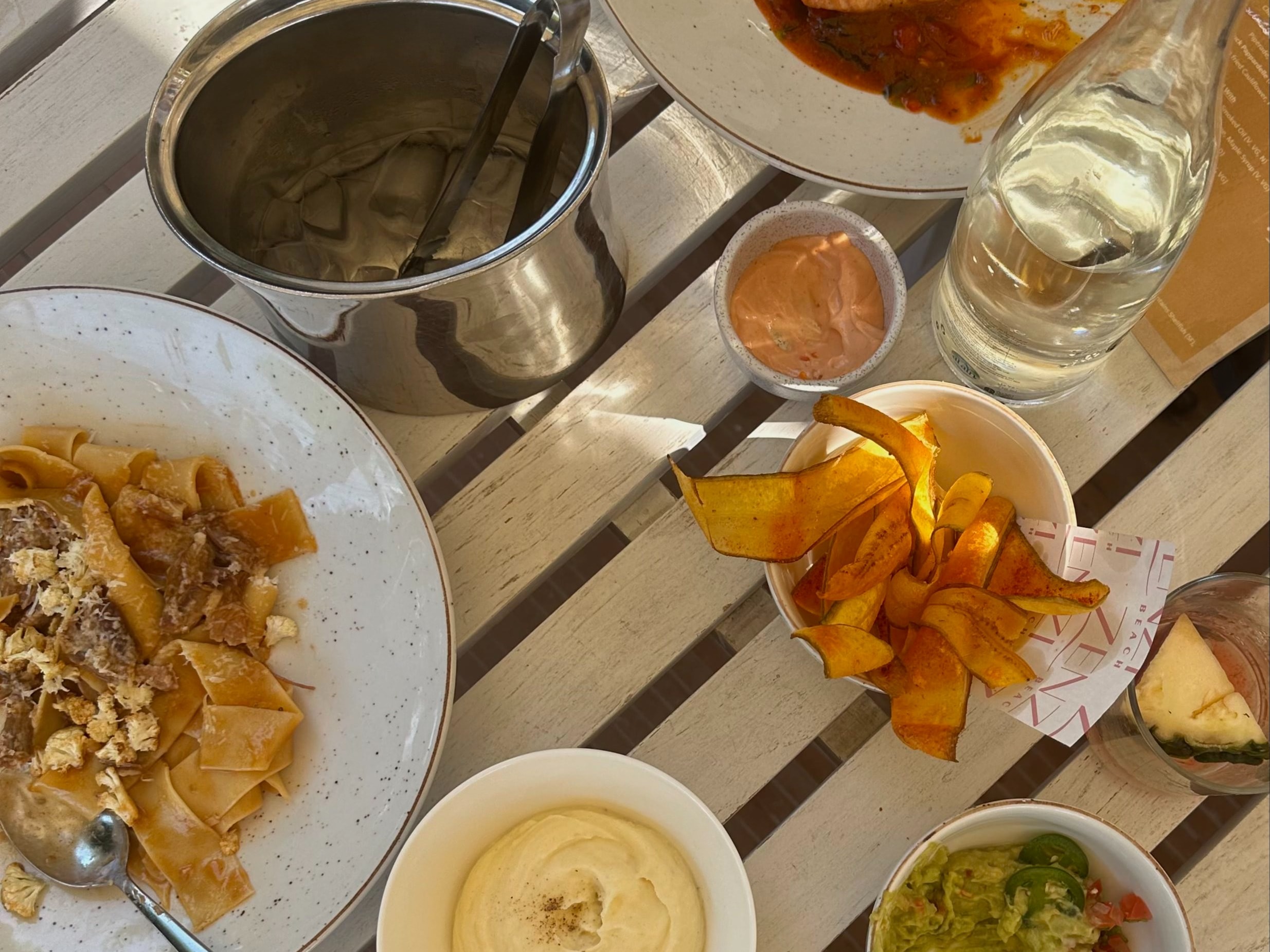 An overhead view of a wooden table with various plates of food, sides and a carafe of water. 