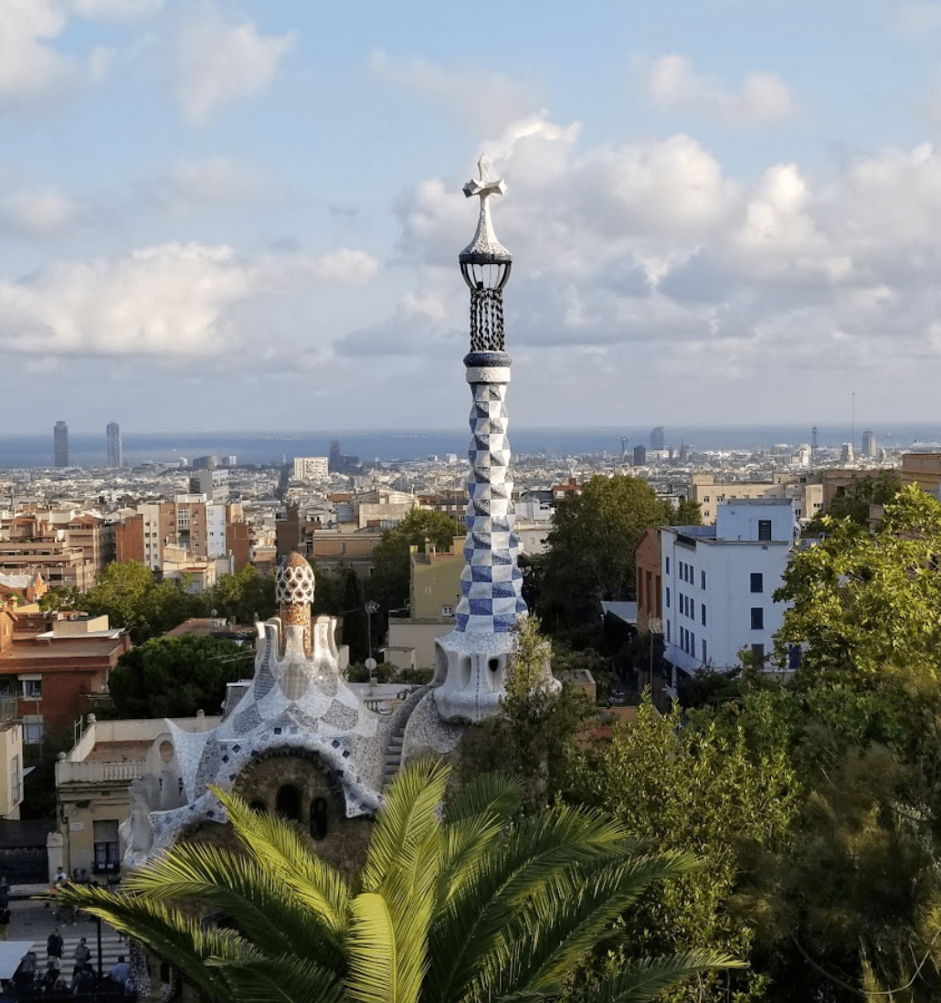 A blue and white spiral in front of a city view in the distance. There are trees and bushes in the forefront. 