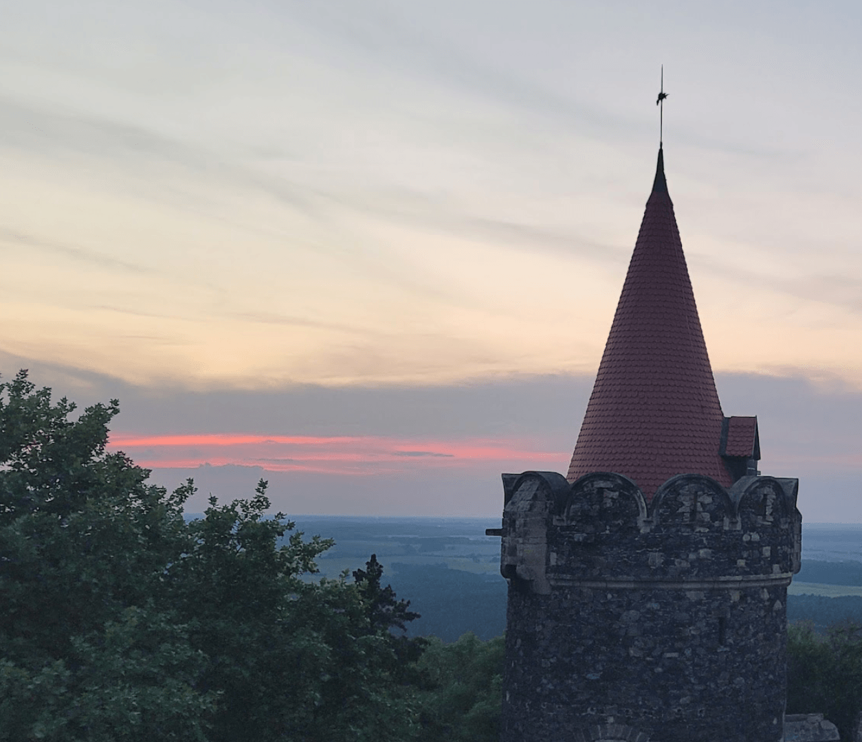 A pink sunset behind trees and a red tower. 