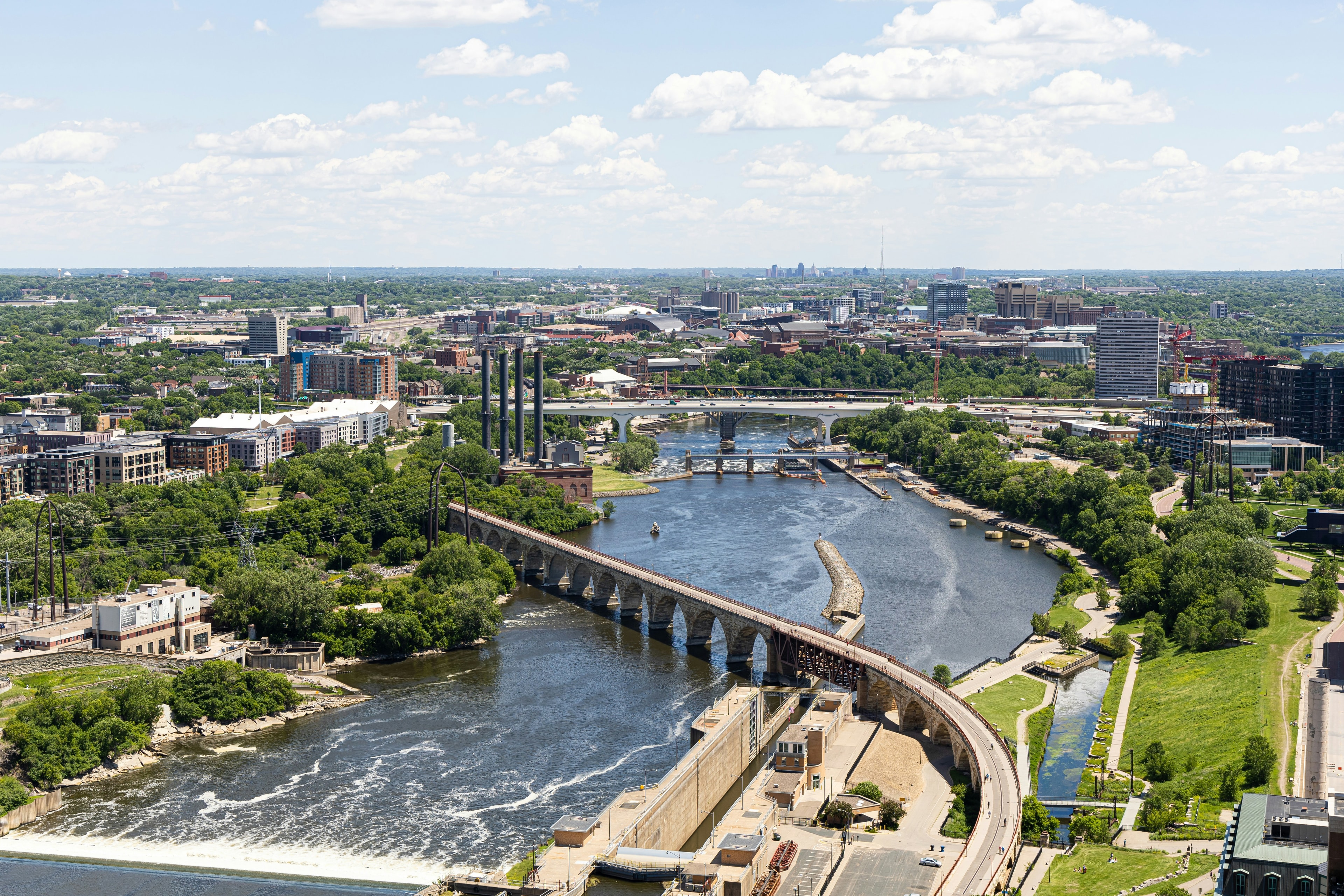 An aerial view of Oxford, Mississippi surrounded by a bustling river, bridge, machinery, trees and city structures. 