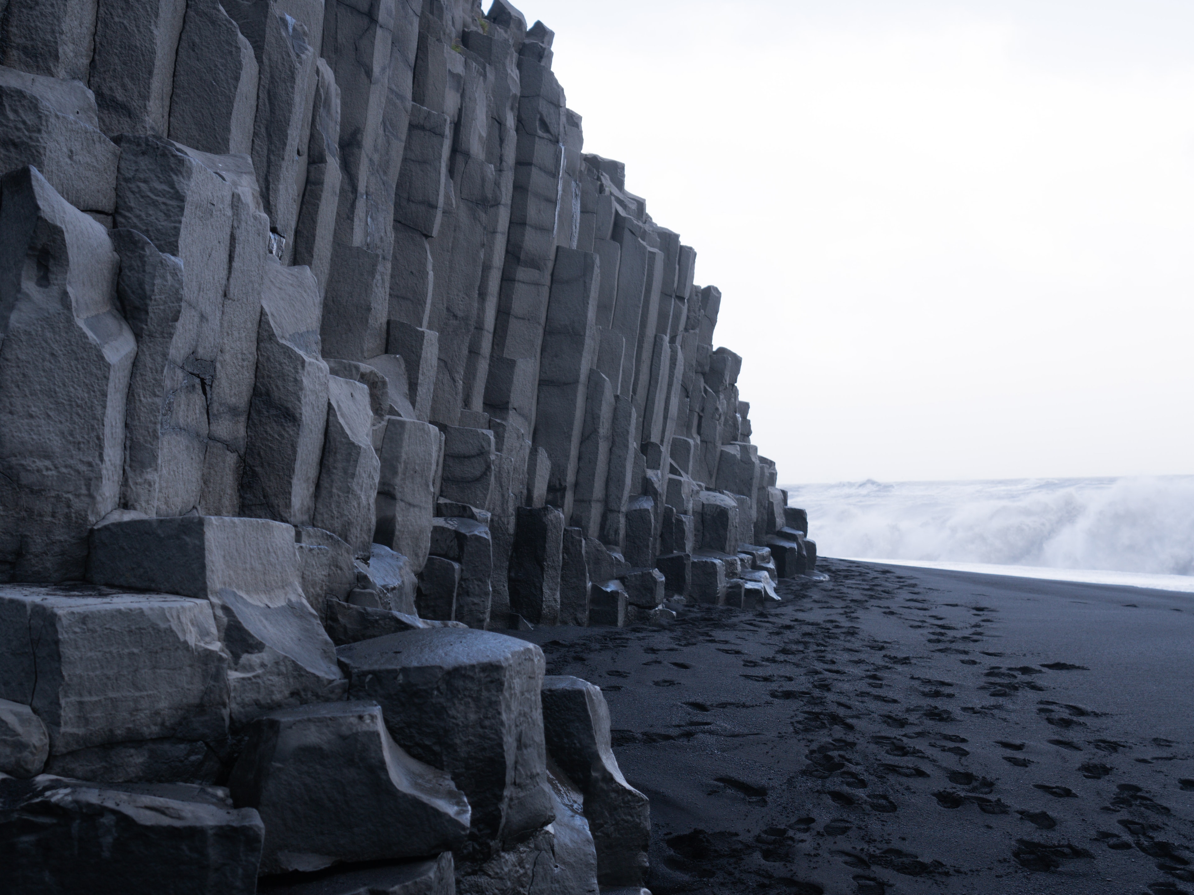 A black sand beach next to a rocky cliff during the daytime