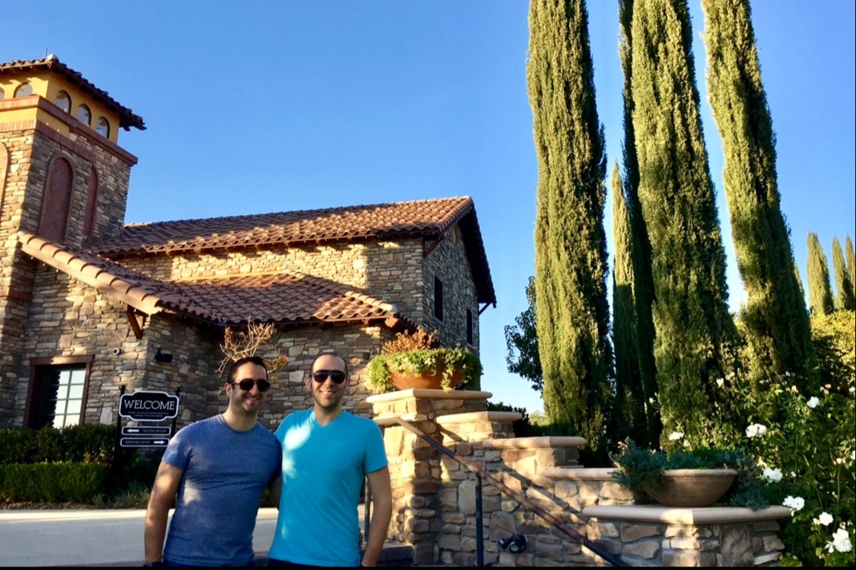 A picture of people posing in front of a stone vineyard taken during the daytime with trees.