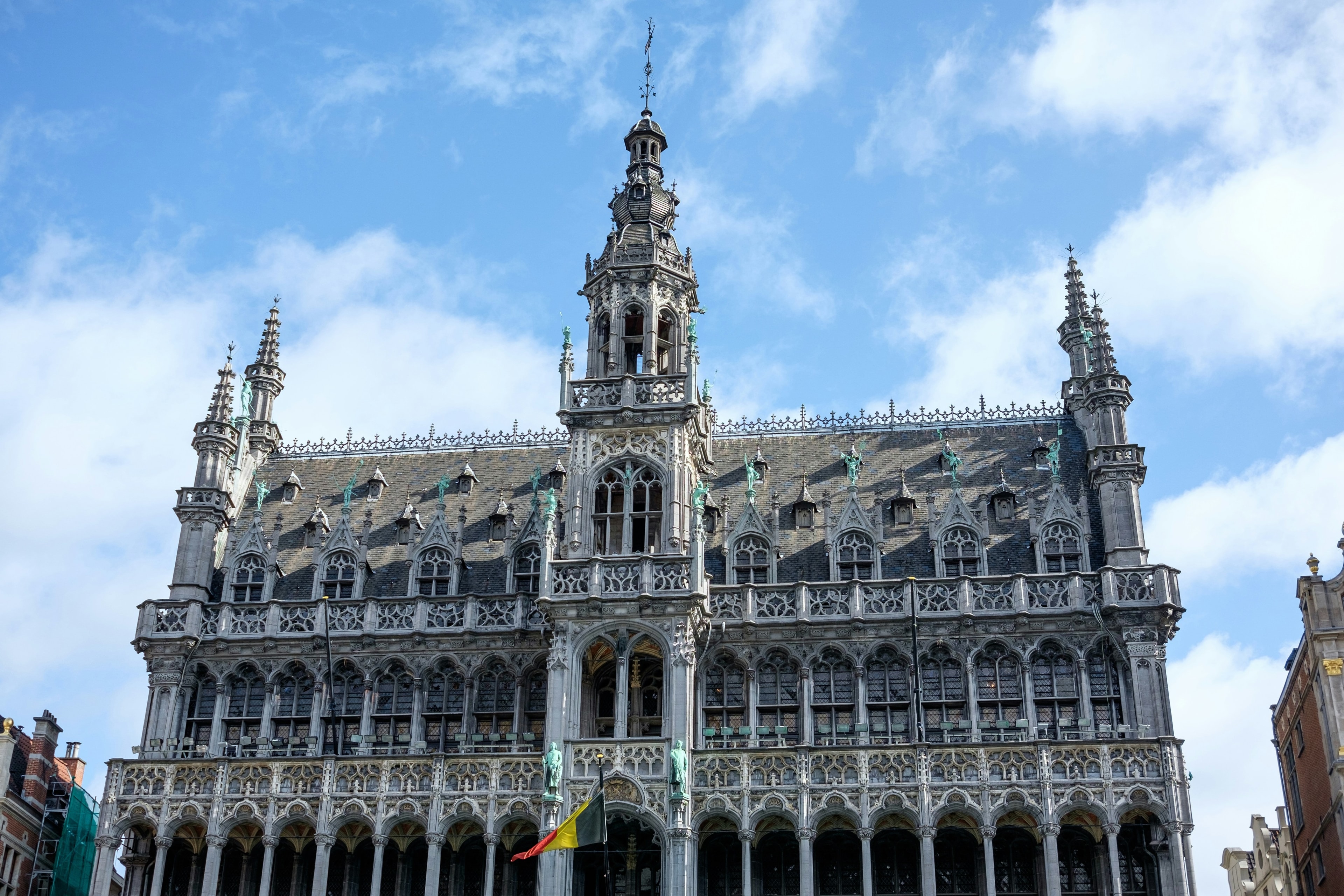 A stone building with luxurious detailing in front of a cloudy blue sky. 