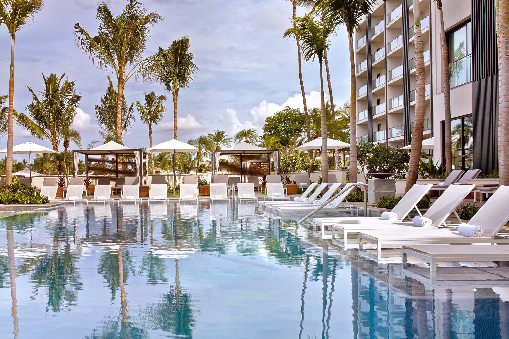 a serene pool surrounded by white lounge chairs and palm trees