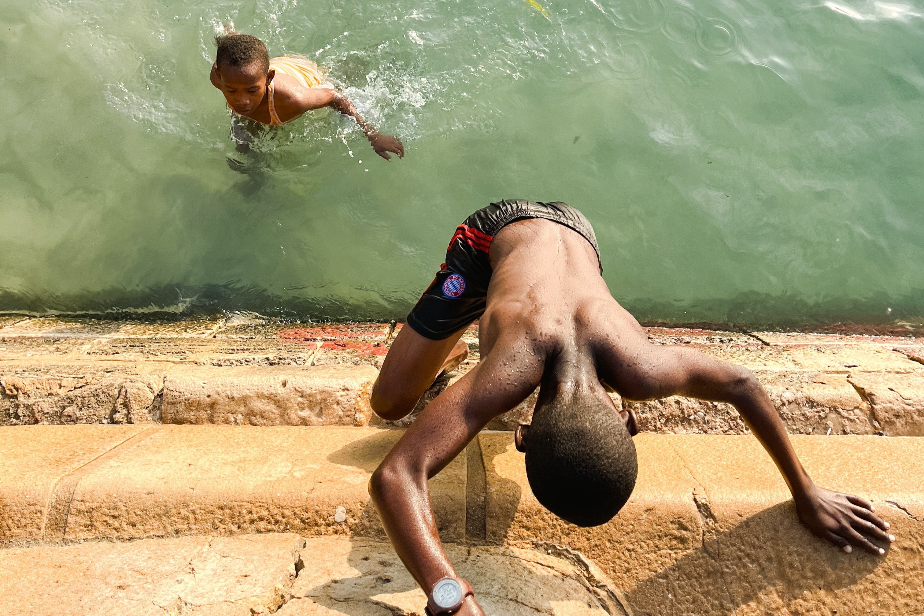 Boys swimming and climbing up a stone wall