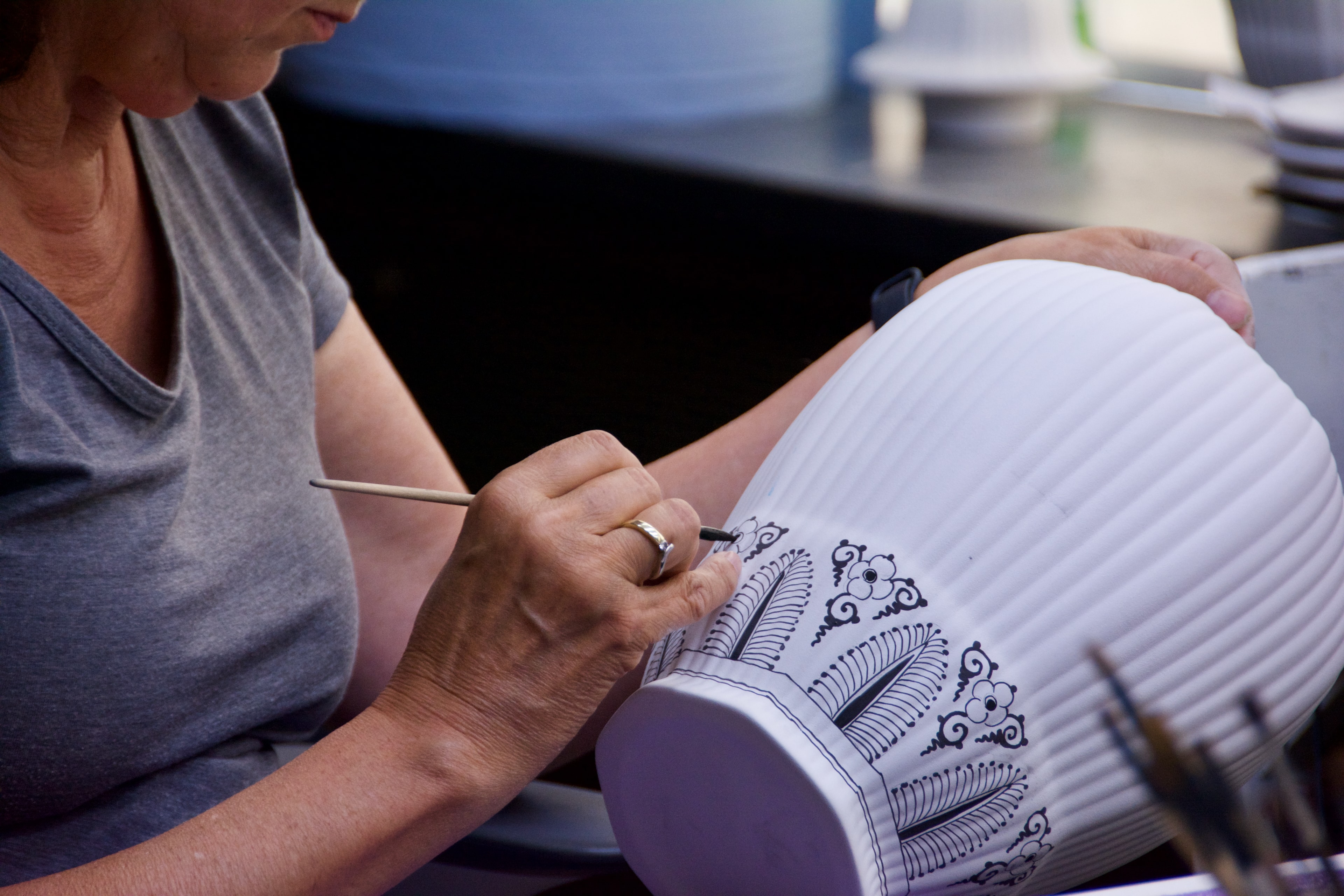 A person painting beautiful artwork on a white pot with blue paint.