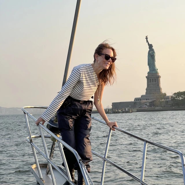 Travel advisor Pamela standing on the front of a boat leaning on the railings with the Statue of Liberty in view.