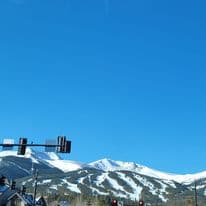 A traffic light with snowy covered mountains in the distance under a clear blue sky