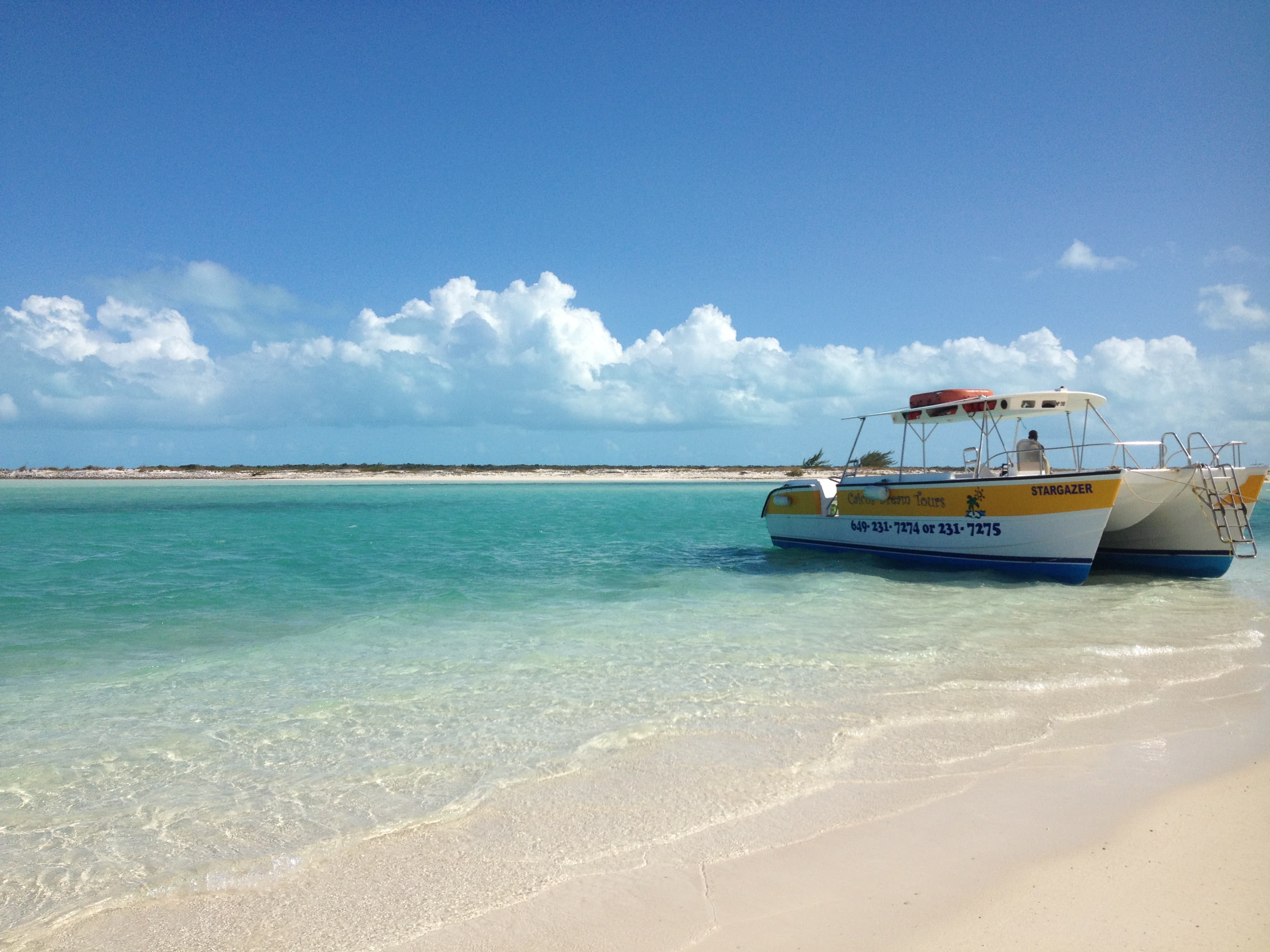 Picture of a yellow and white boat at the shoreline against white sand and crystal blue water