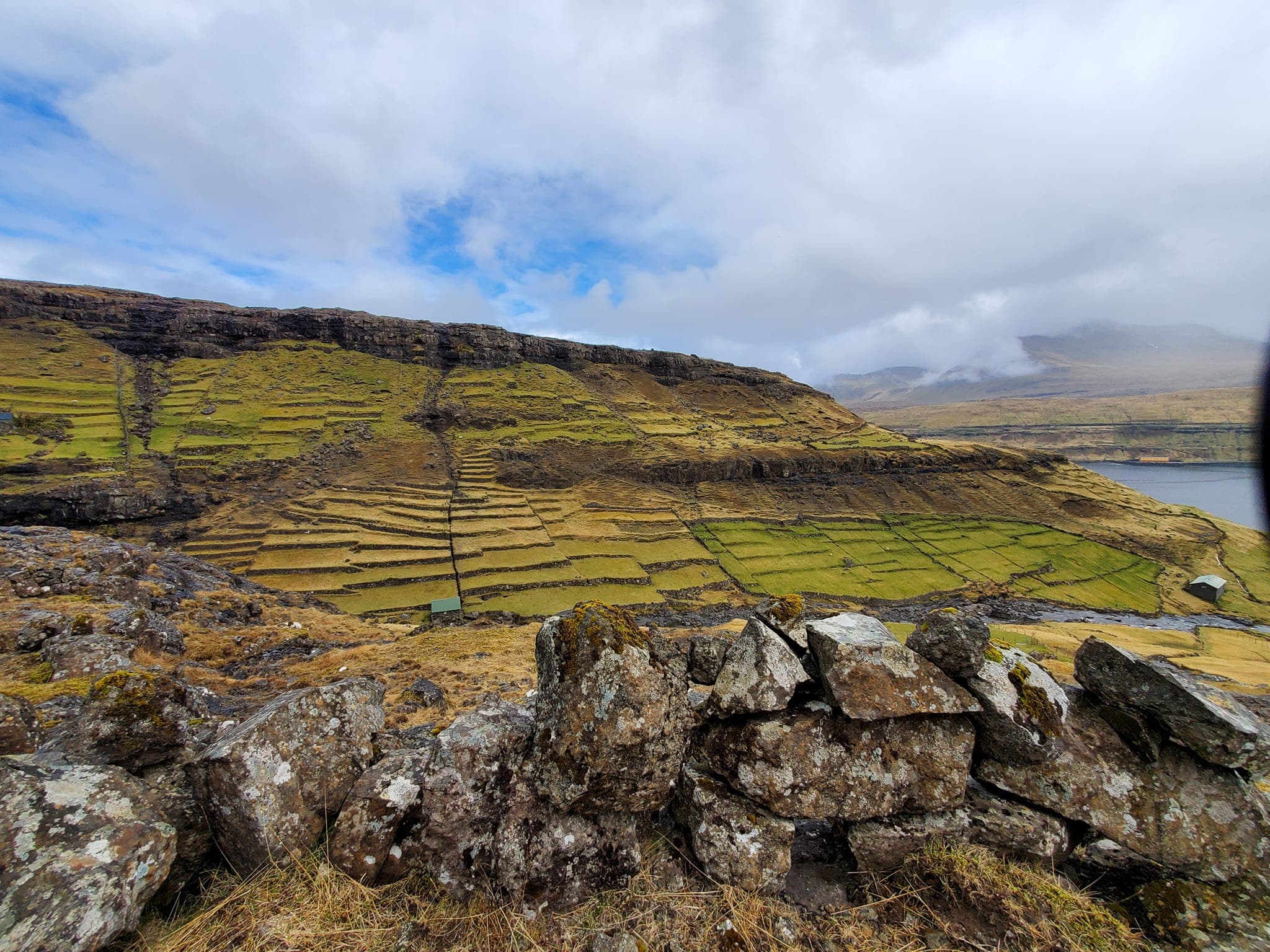 Green grass and rocky mountain view with a sea in the background.
