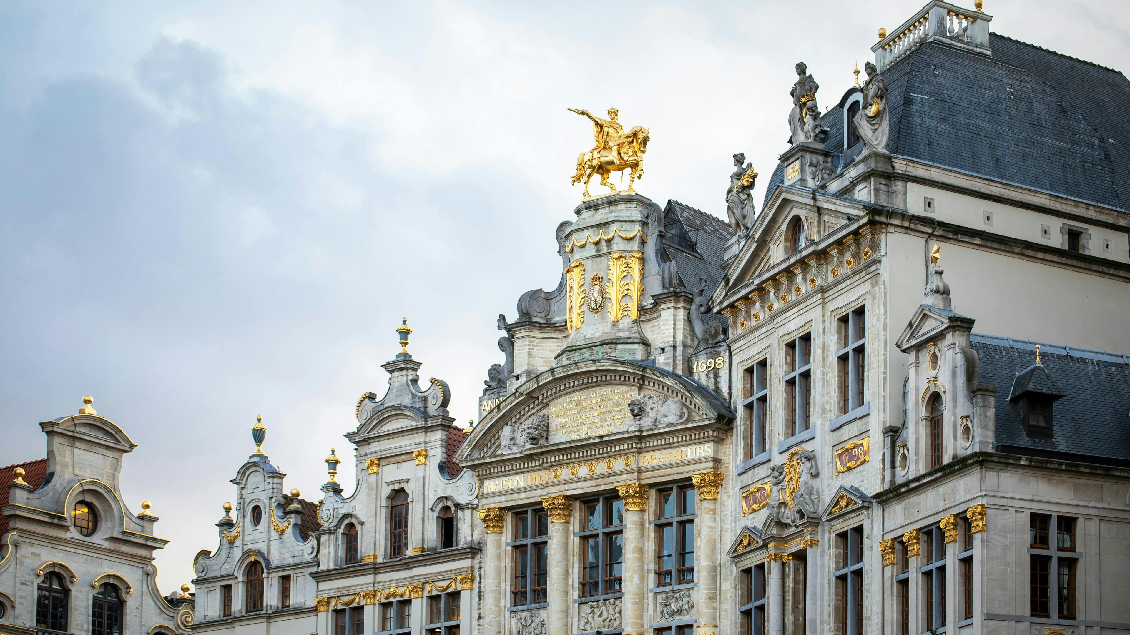 A side view of the ornate concrete Grand Place in Brussels with a gold statue on top.
