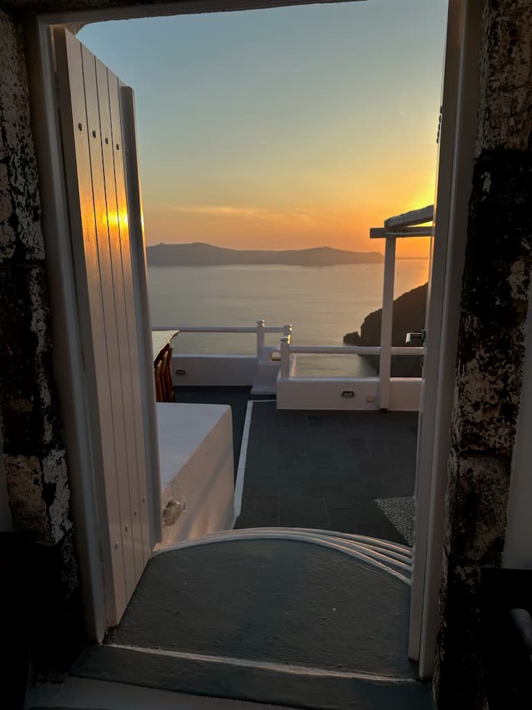 An open window looking out onto a stone patio, water and sunset with mountains in the distance