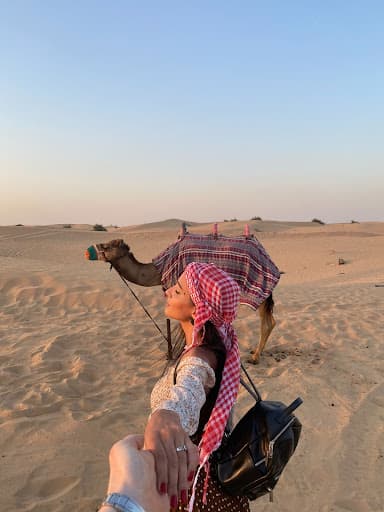 Girl next to camel in desert.
