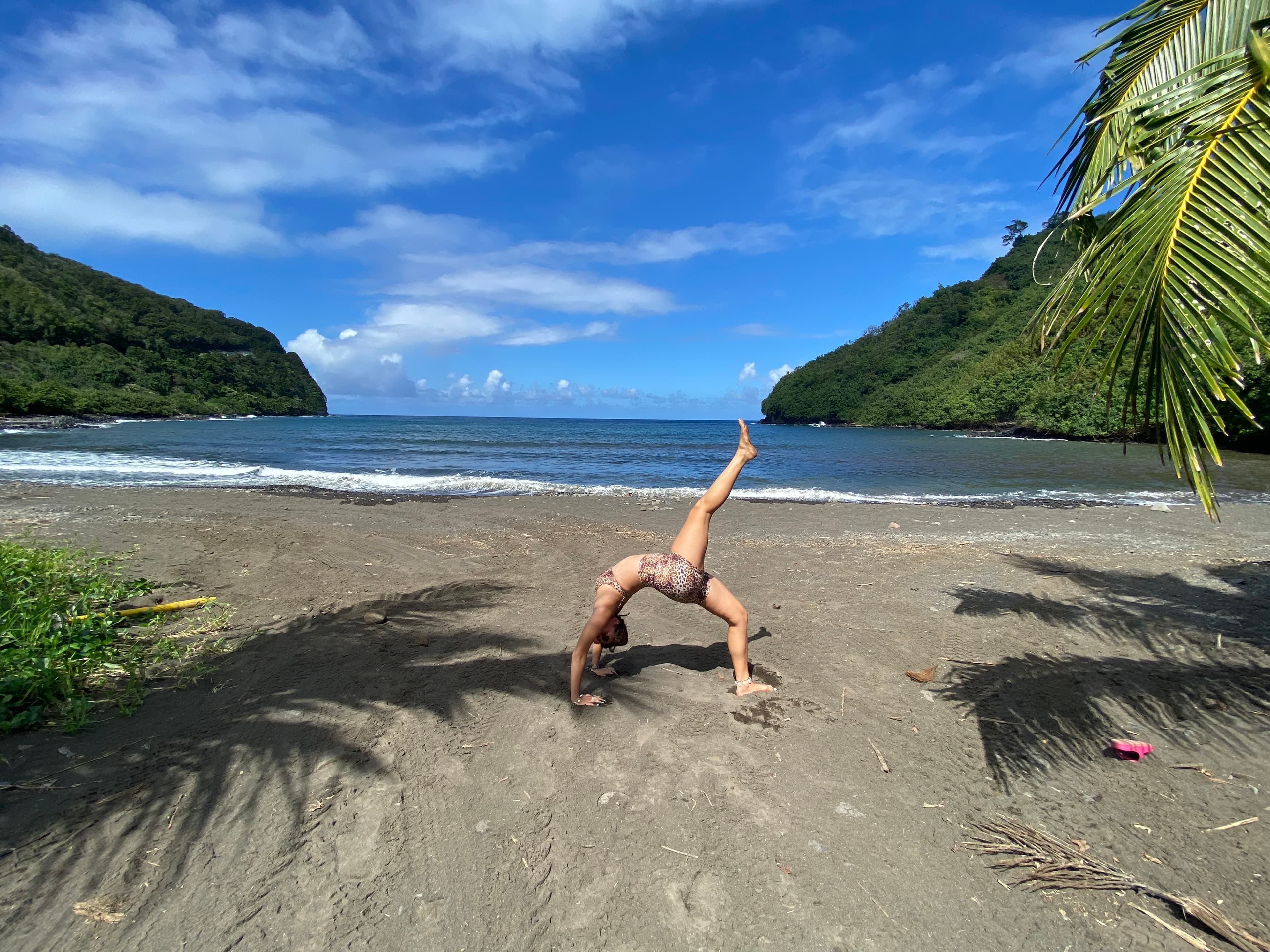 Annemarie doing a yoga pose on the beach outside at Honomanū Bay with water and volcanoes in the background.