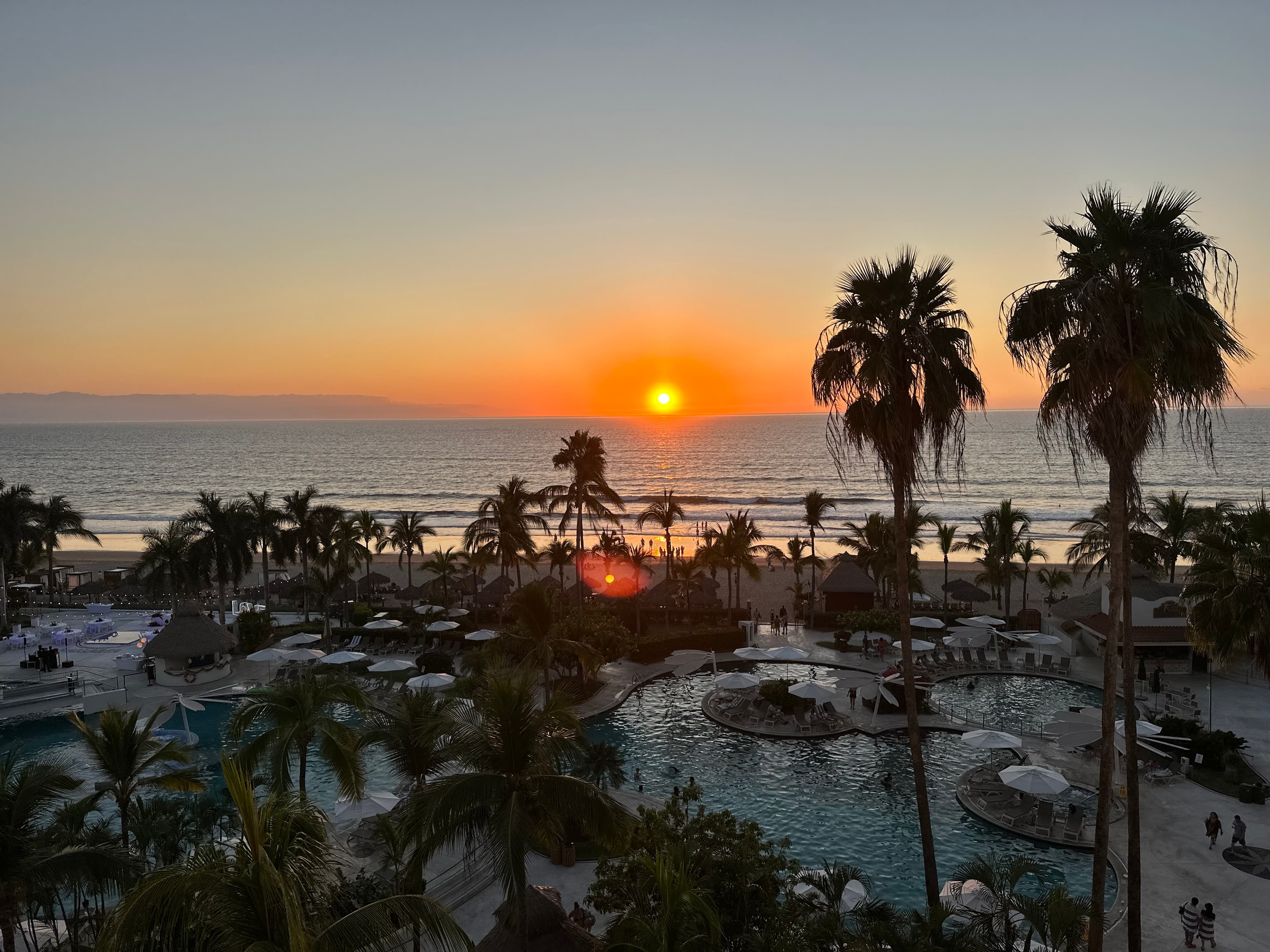 A picture of a beautiful resort at sunset with swimming pools, palm trees and the sea in view