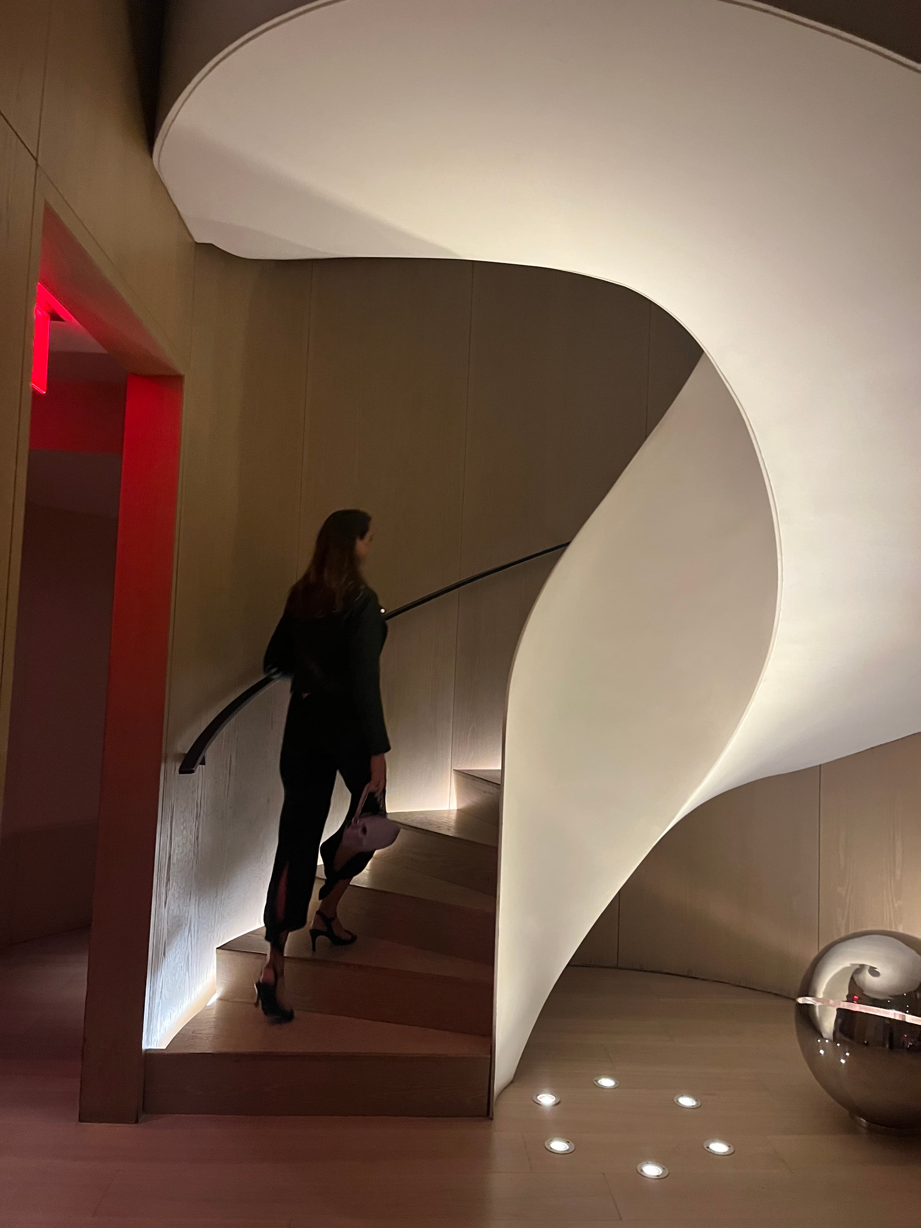 A person walking up an abstract white staircase with a red lit doorway to the left of them