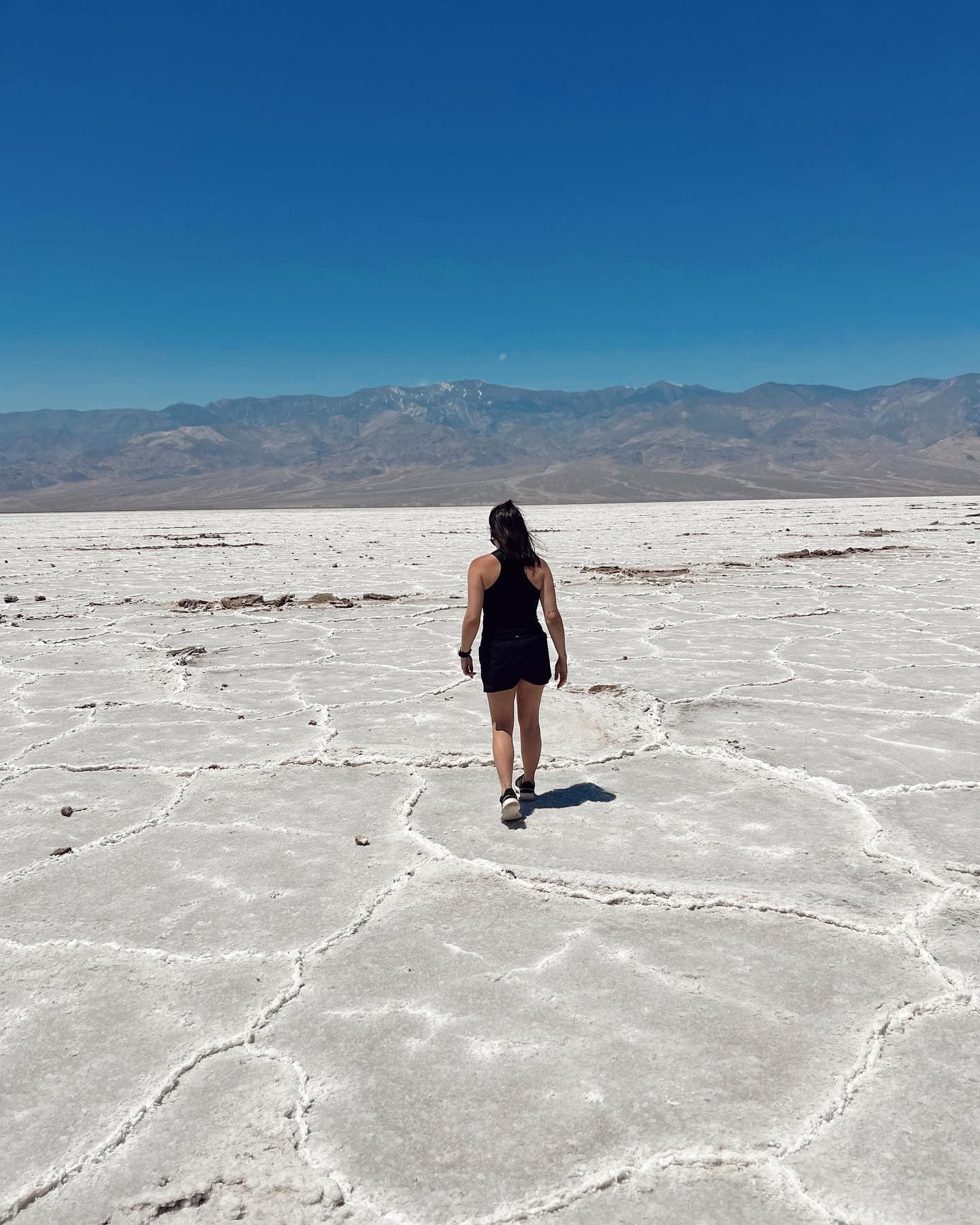 A girl walking on white salt flats with mountains in the background and a blue sky