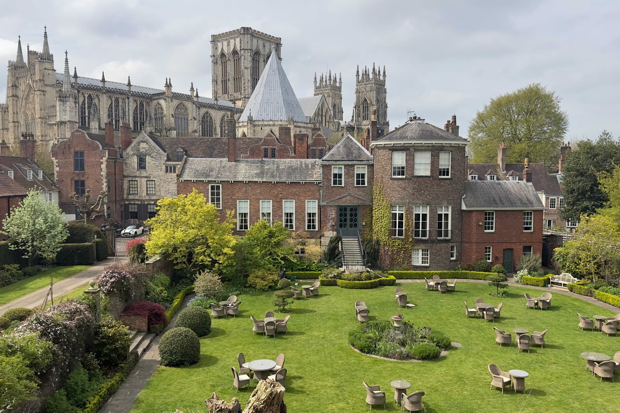 Tables and chairs dot a green lawn in front of a handsome stone castle.