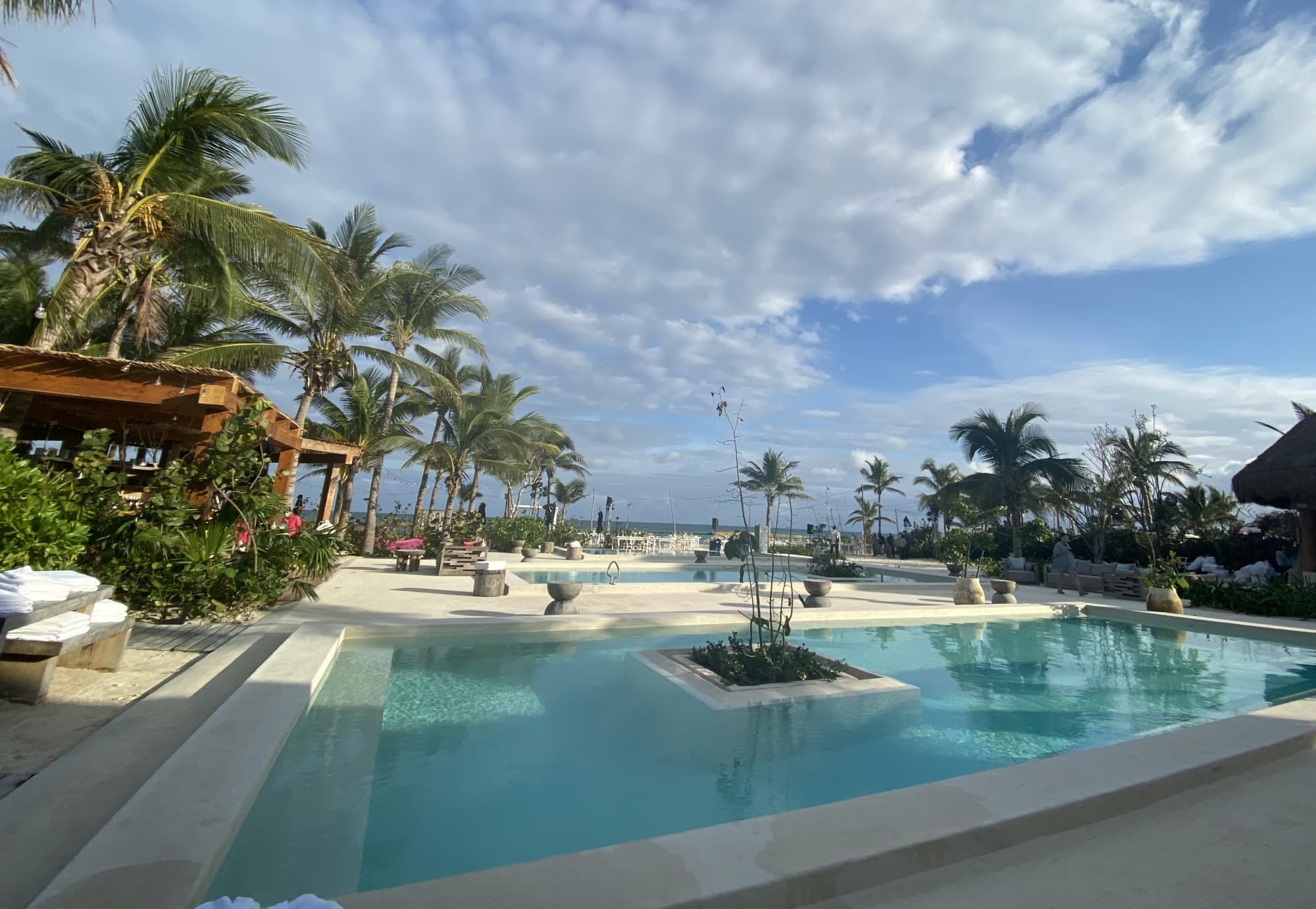 a large pool surrounded by tropical plants and the ocean in the distance