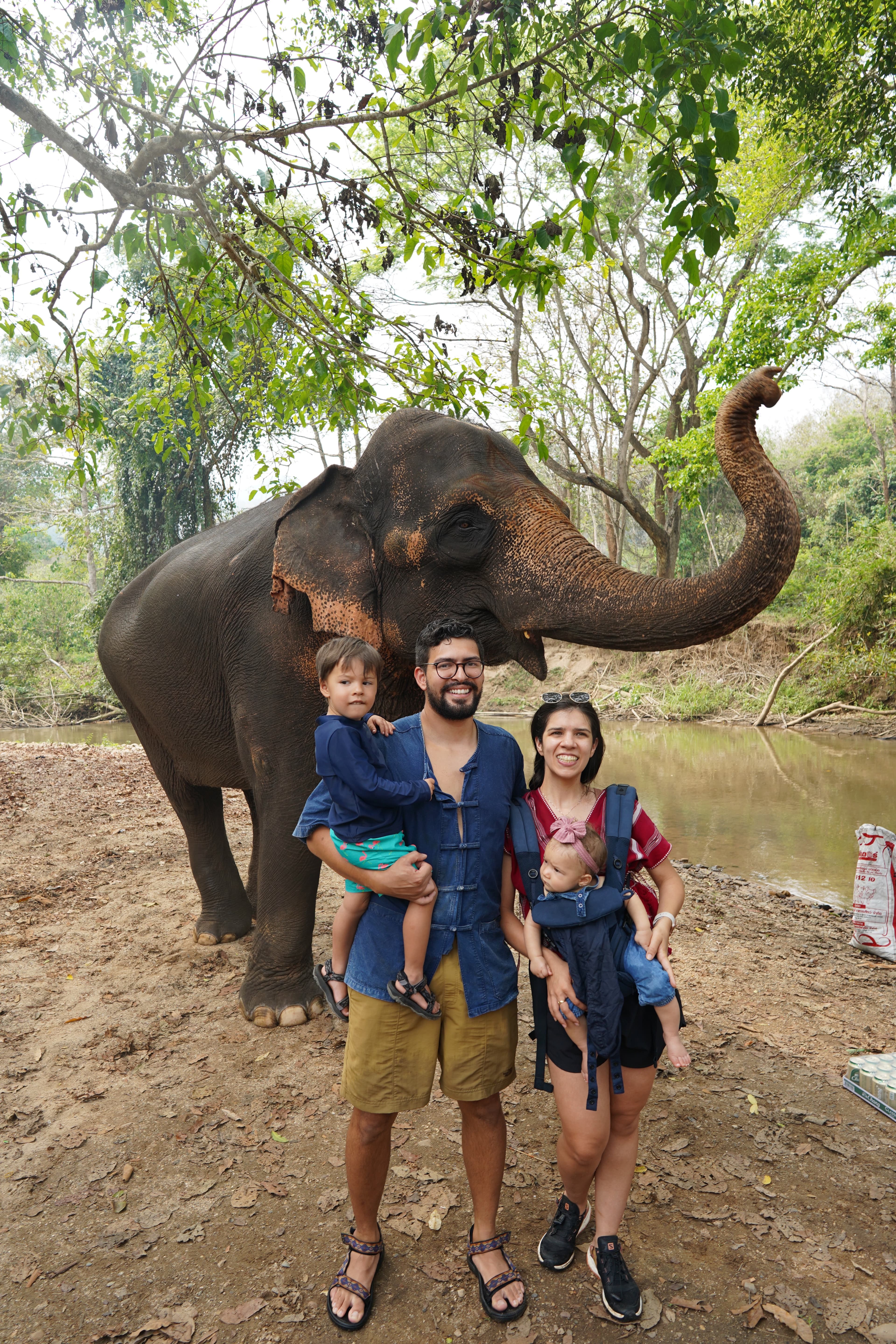 Maria, husband, and two kids posing in front of an elephant with its trunk outstretched.