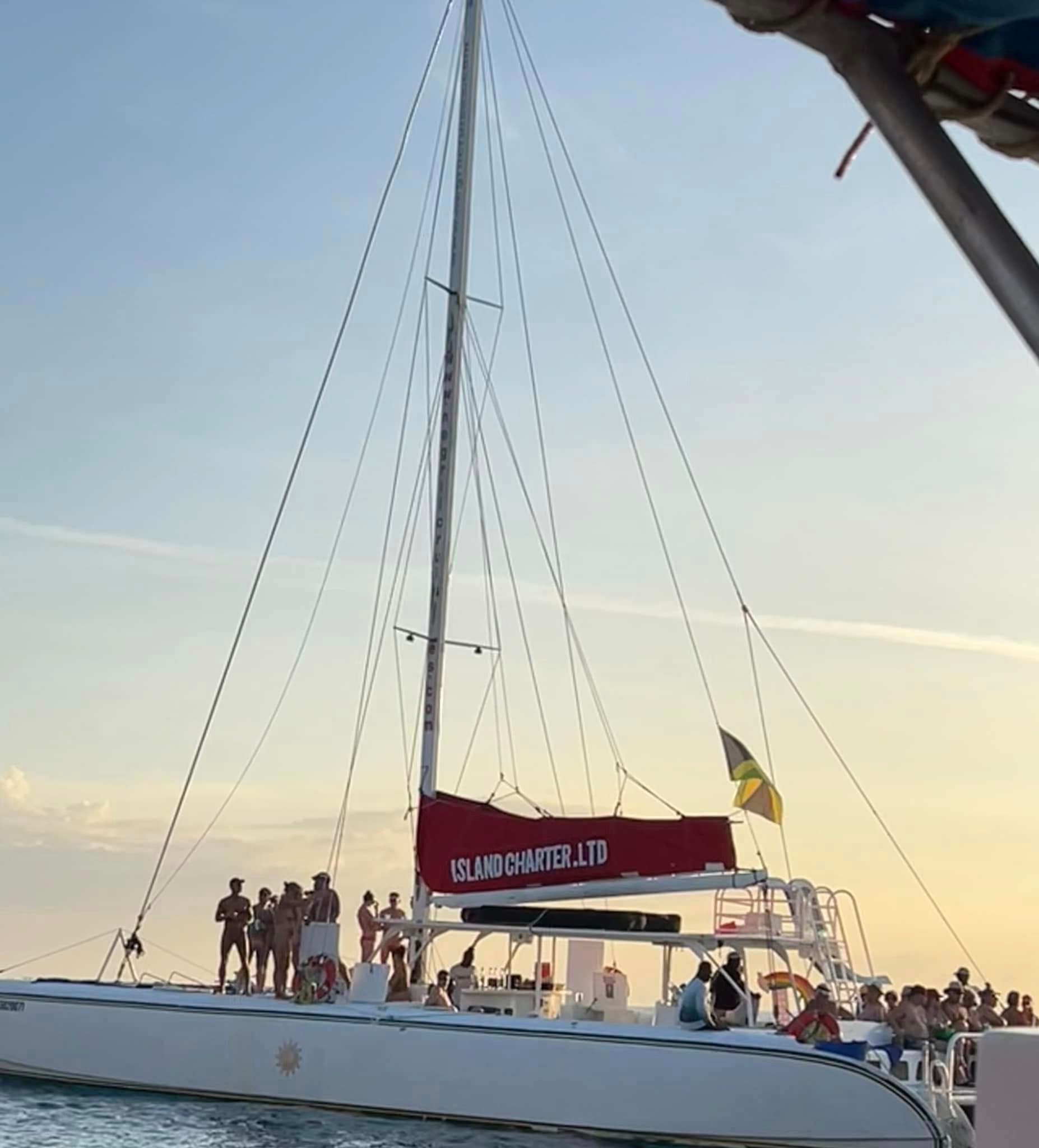 A white sailboat with people on it sailing on the water at sunset