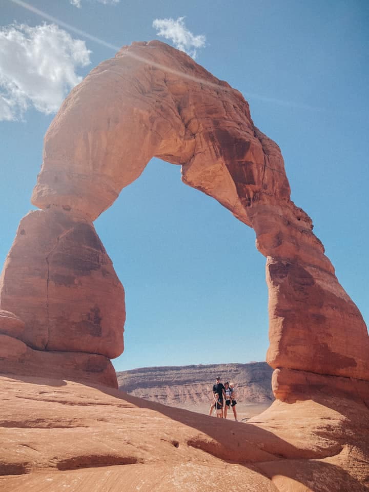Two people standing underneath a rock-formed arch called the Delicate Arch in Utah