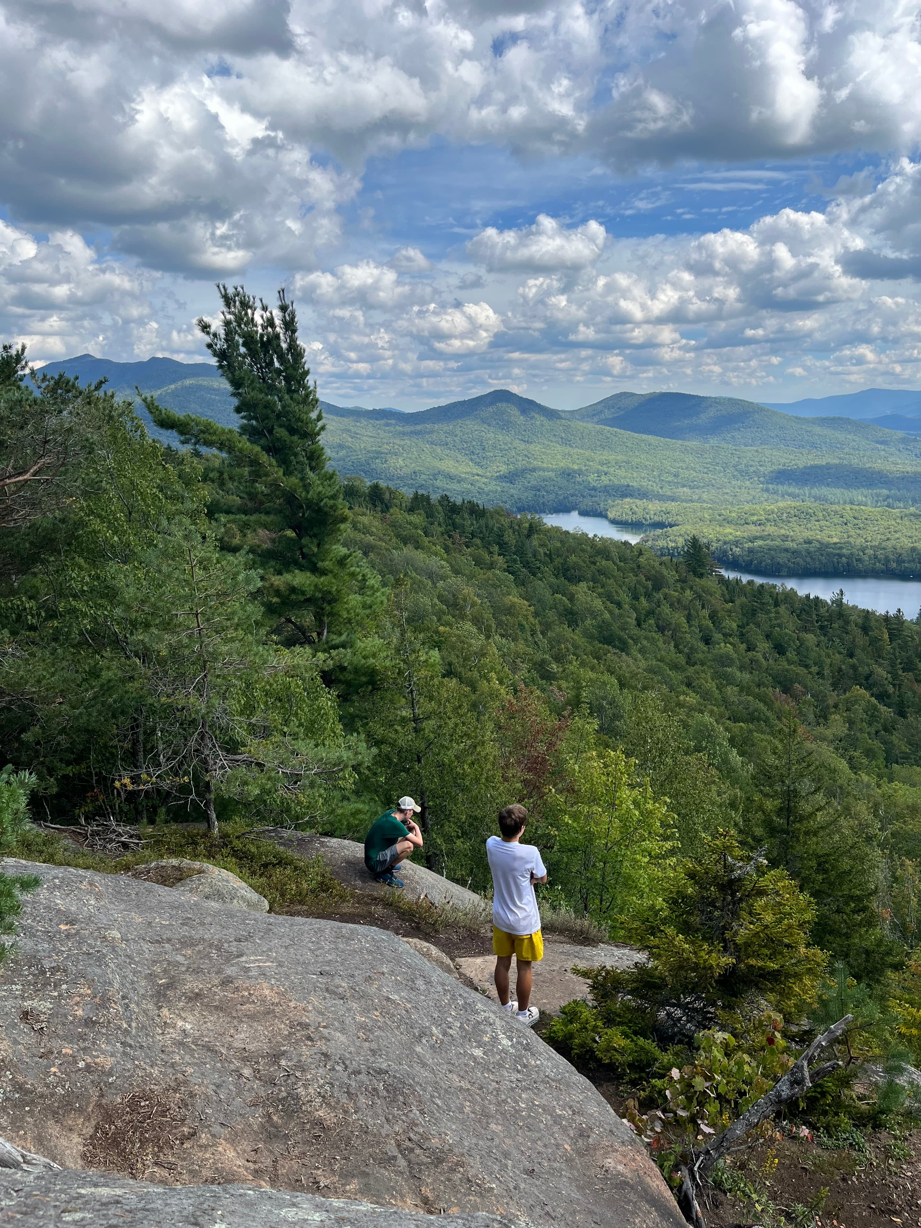 Christie sitting amidst the mountains with a friend looking at the view below.