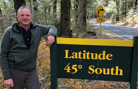 Ken standing in front of a road sign that reads 'Latitude 45º South' in a forest setting