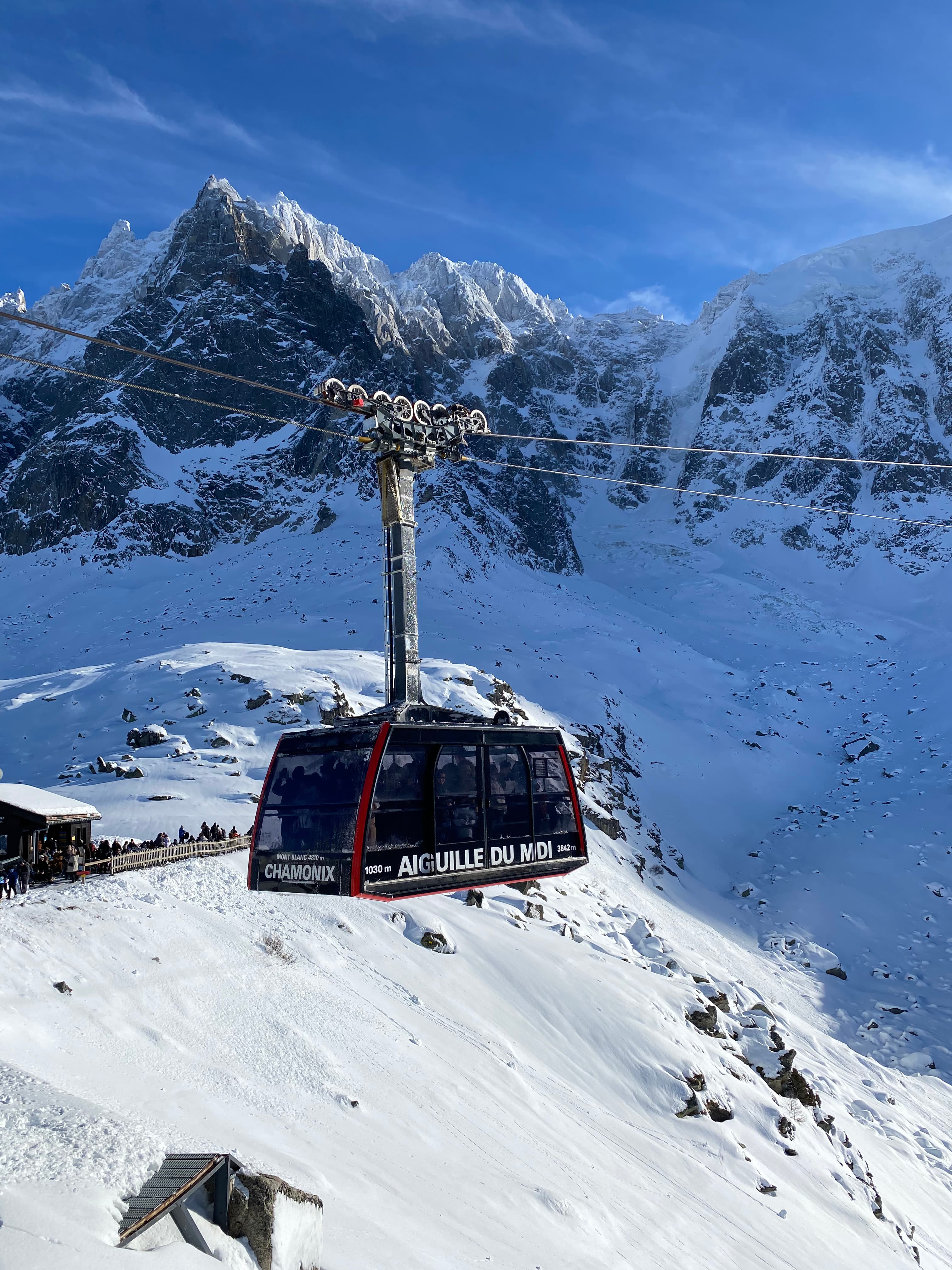 Picture of a red ski lift traveling above snowy mountains under the cloudy and blue sky