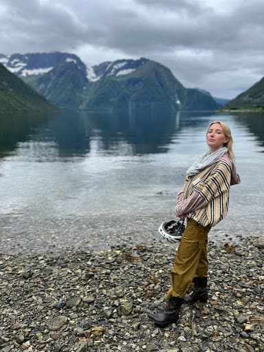 A girl standing on lake next to mountains.