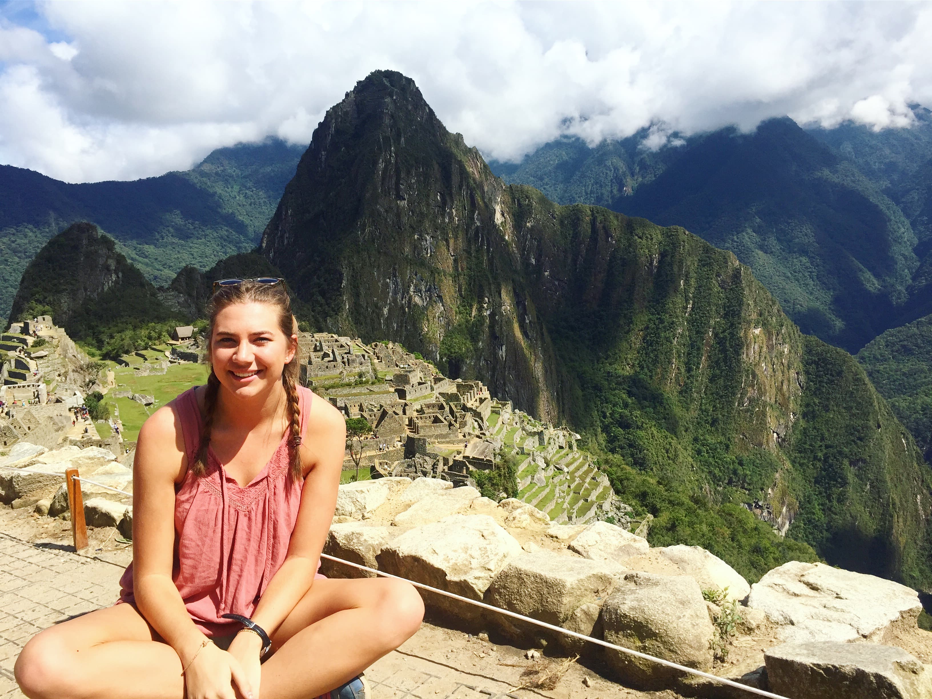 Lauren sitting high up above the historic sanctuary of Machu Picchu, Peru on a sunny day.