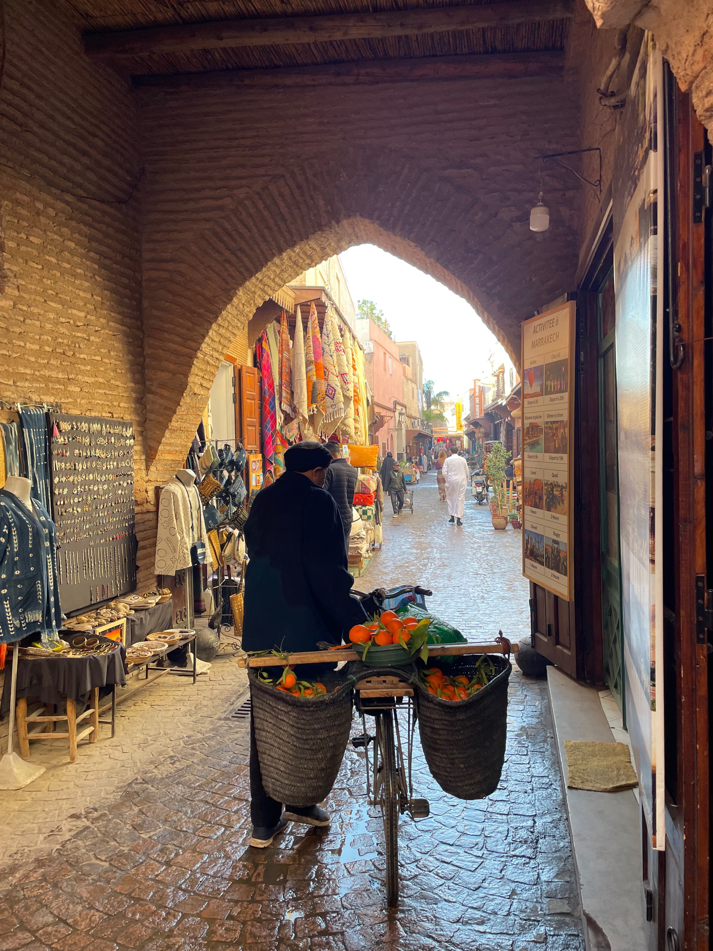A man walking a bicycle with baskets of oranges through a brick alleyway on a Morocco 7 day itinerary.