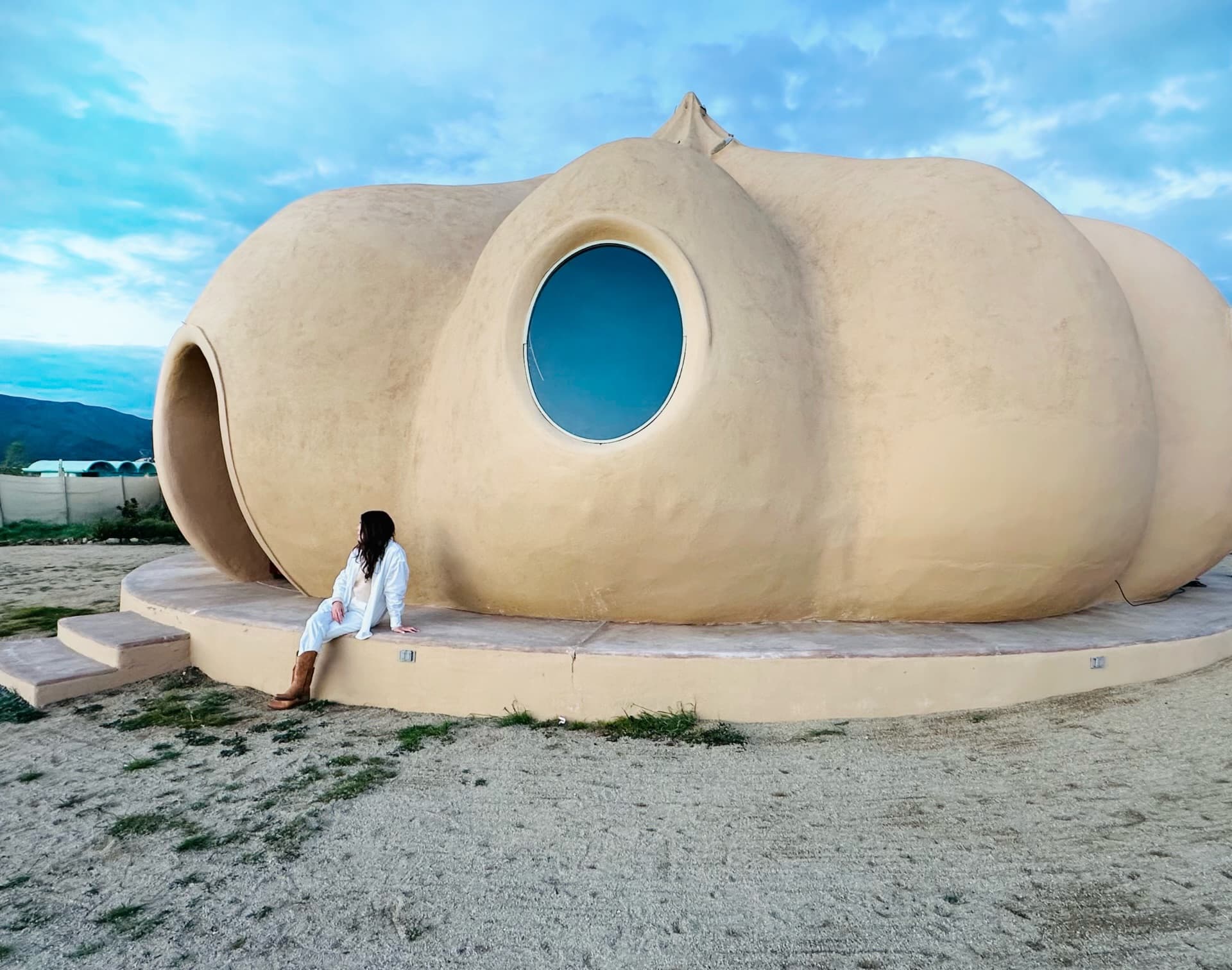 Gabby wearing a white outfit and posing seated in front of the Valle de Guadalupe