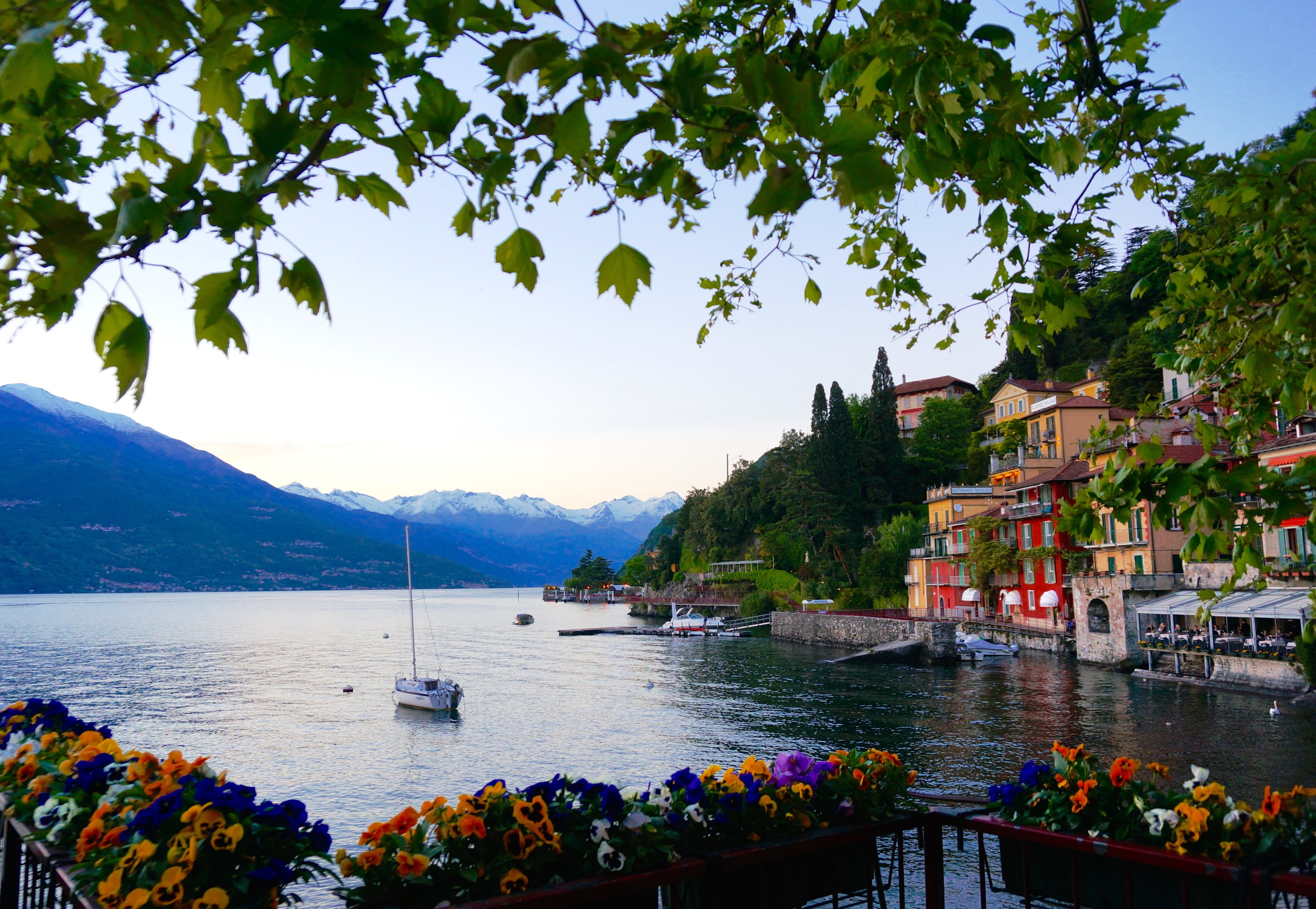 A view of Lake Como from a floral terrace with a boat, mountains and colorful neighborhood in the distance