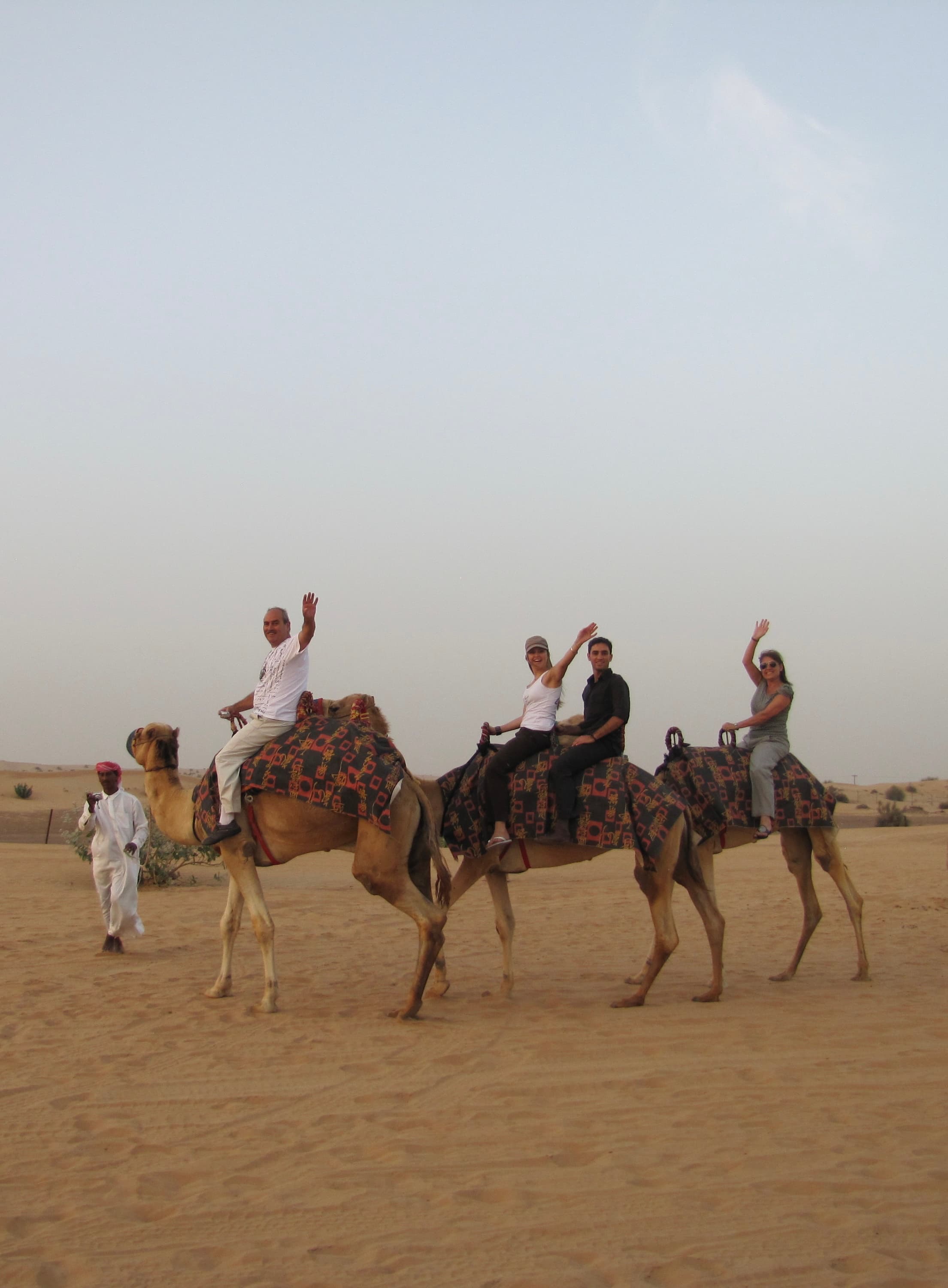 A photo of three people on a camels on a sand dune.