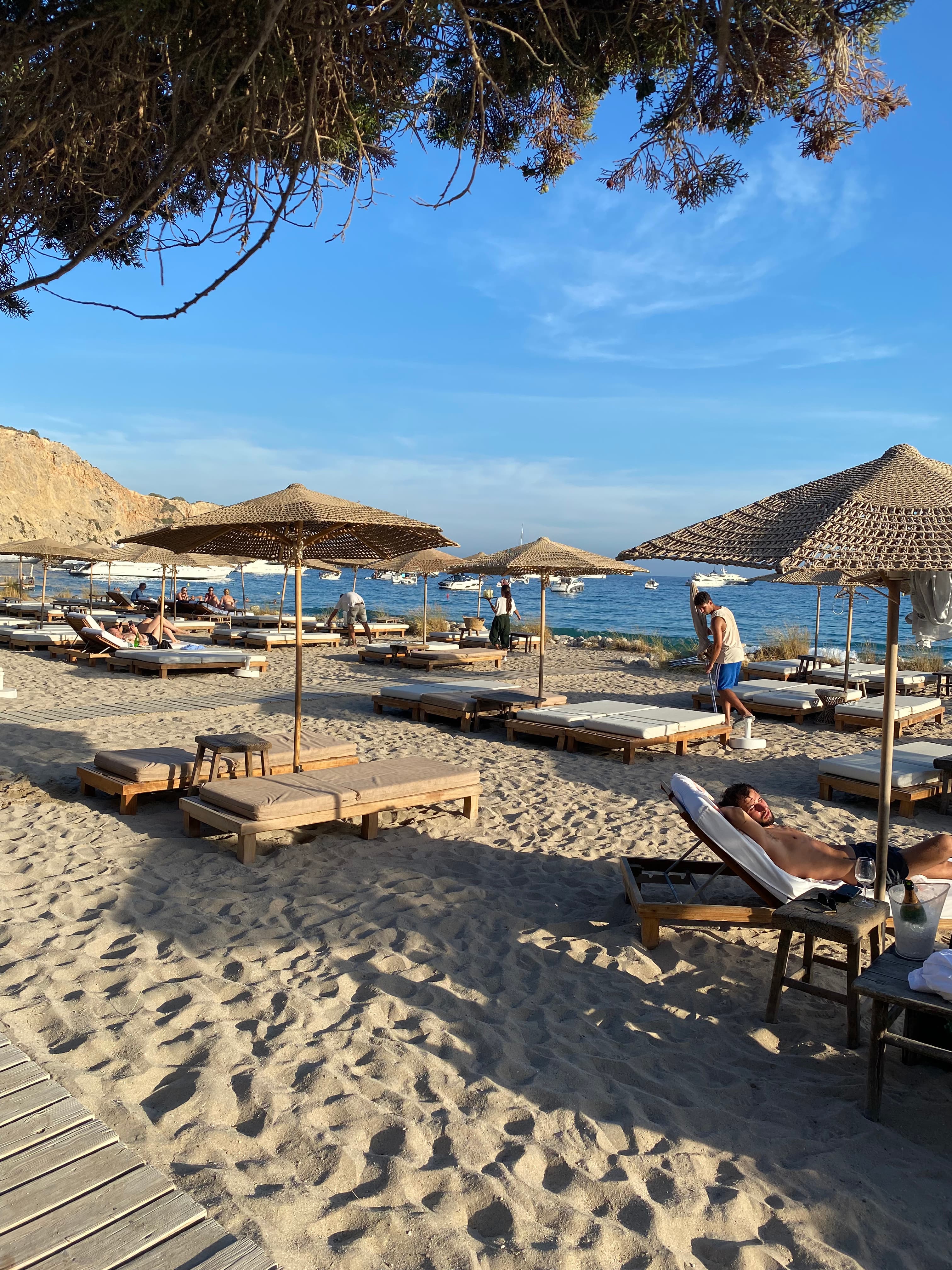 A picture of lounge chairs and straw umbrellas on the beach with the ocean in the background