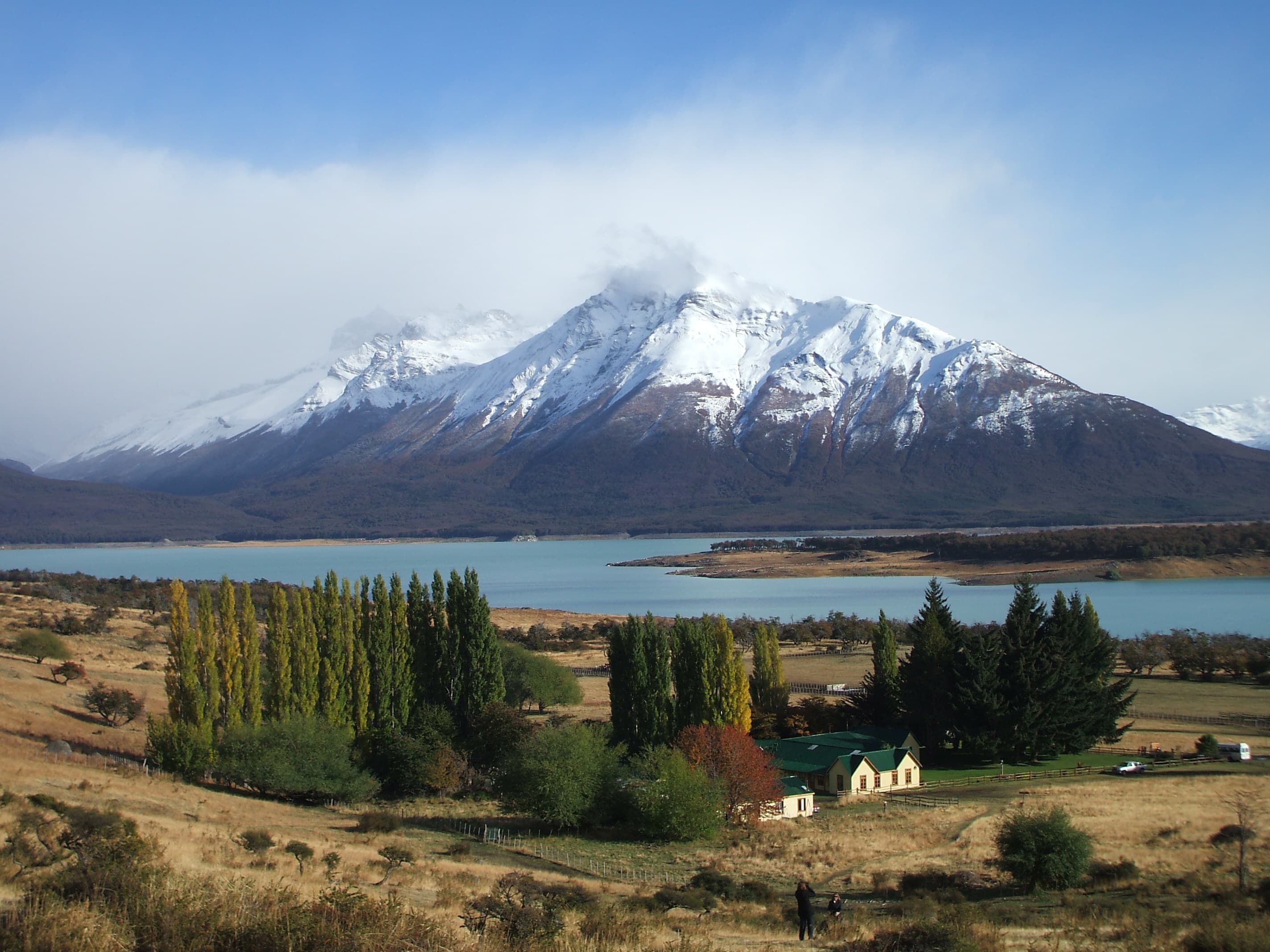 A picture of a snow-capped mountain with blue lake and green trees.