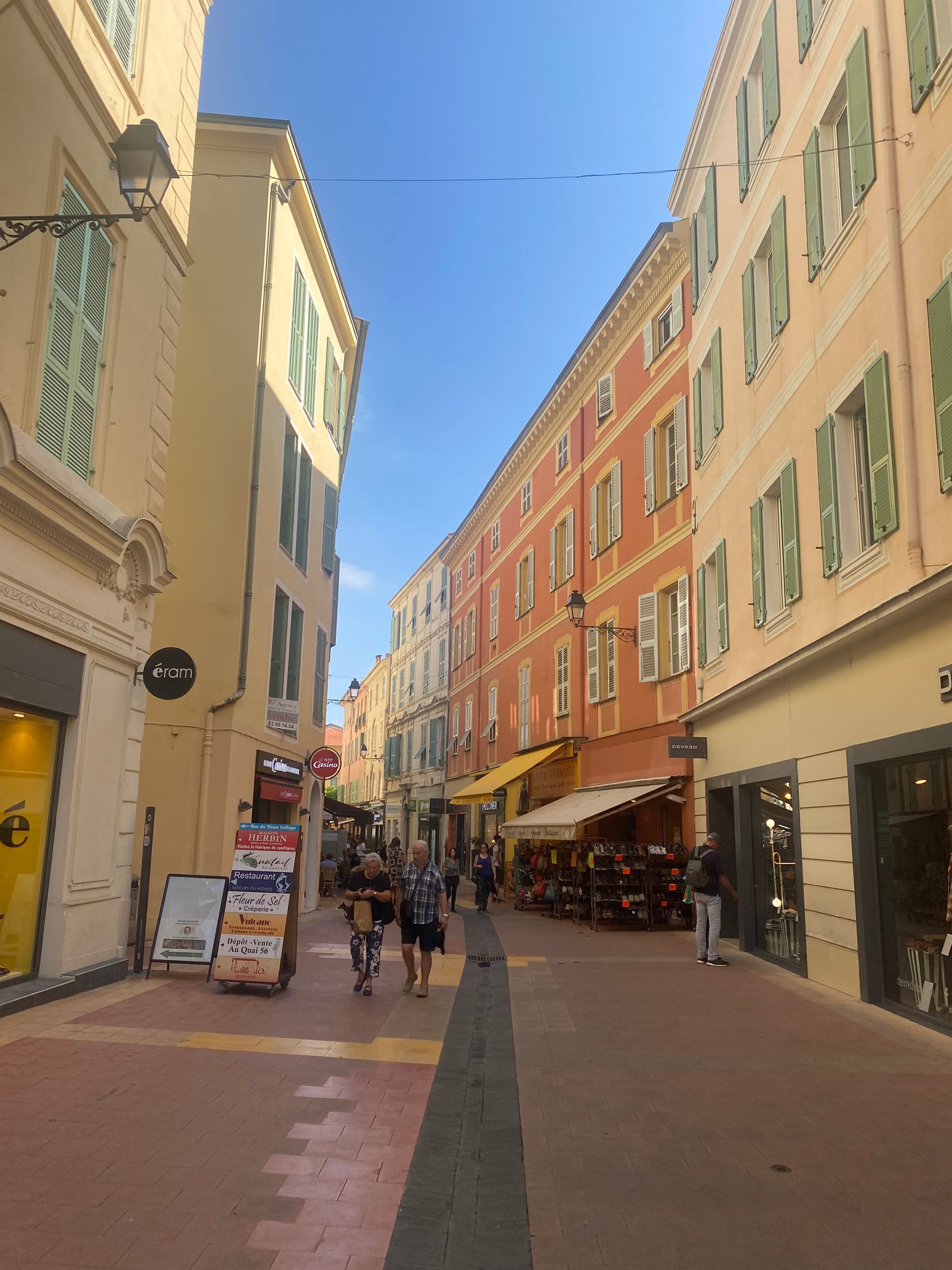 A European road with tan and red buildings and people walking down the street.