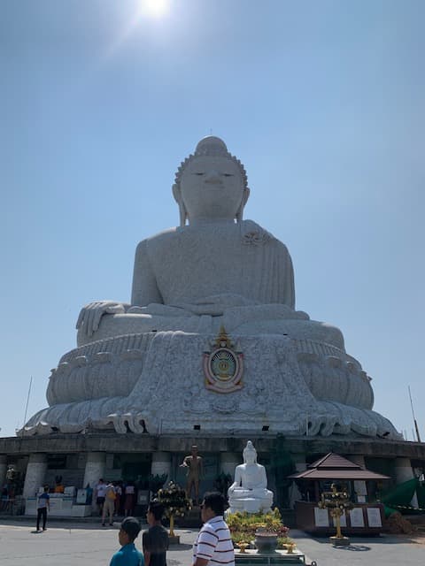 A large white statue of Buddha with clear skies and the sun shining.