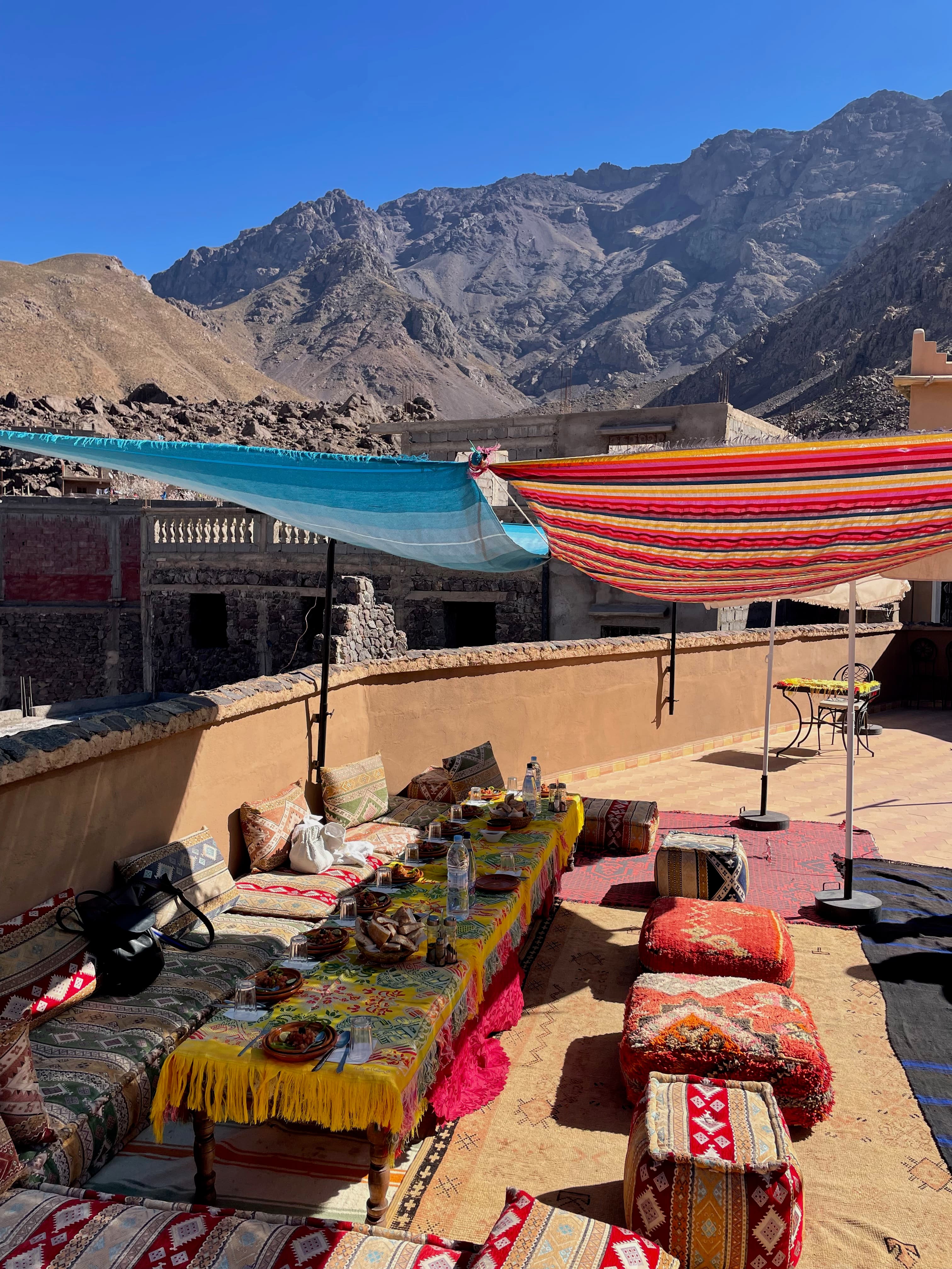A rooftop patio in the Atlas Mountains with colorful tables and floor cushions on day 3 of a Morocco 7 day itinerary.