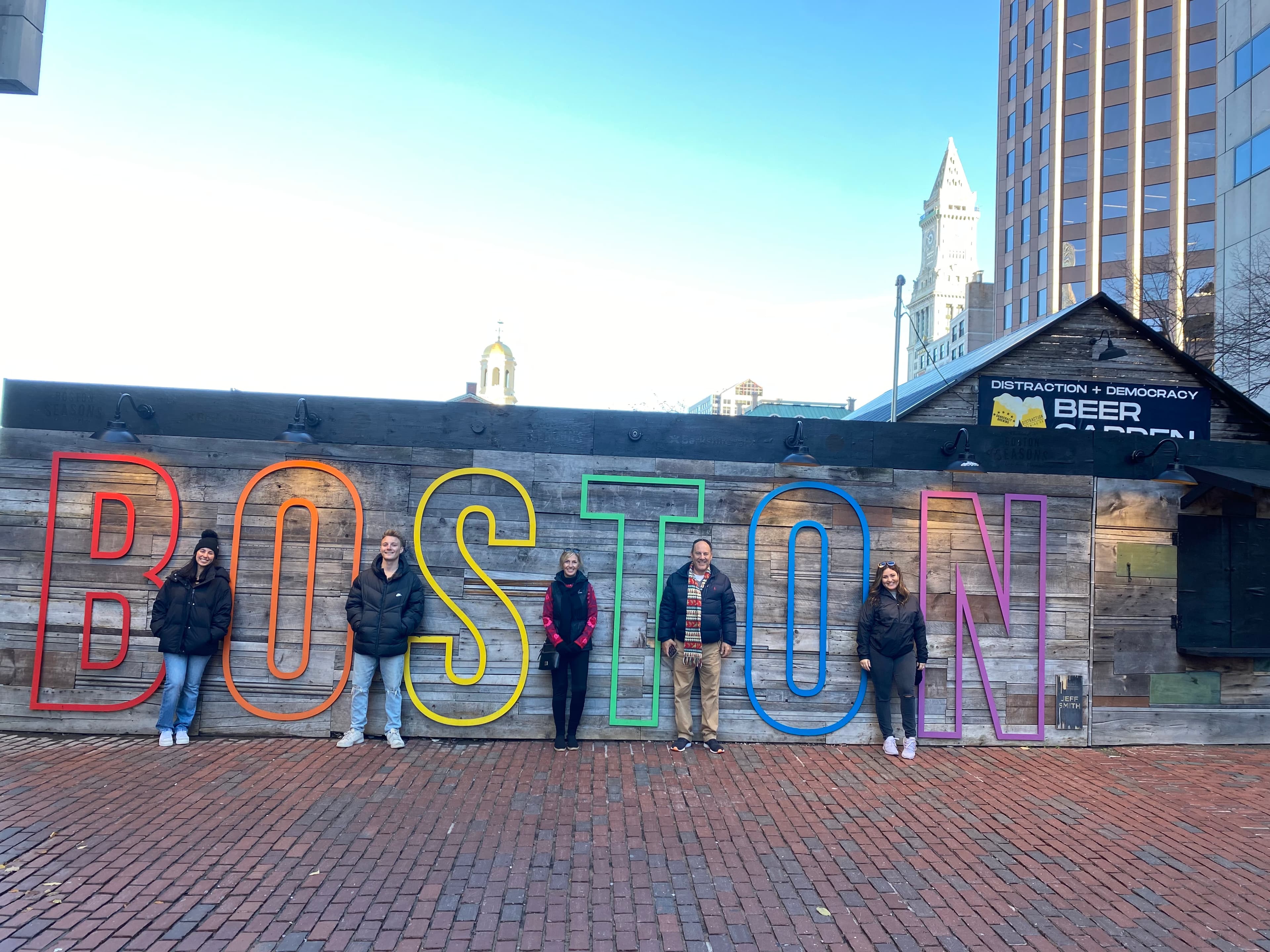 Picture of people standing in front of a colorful Boston sign set against a brick wall