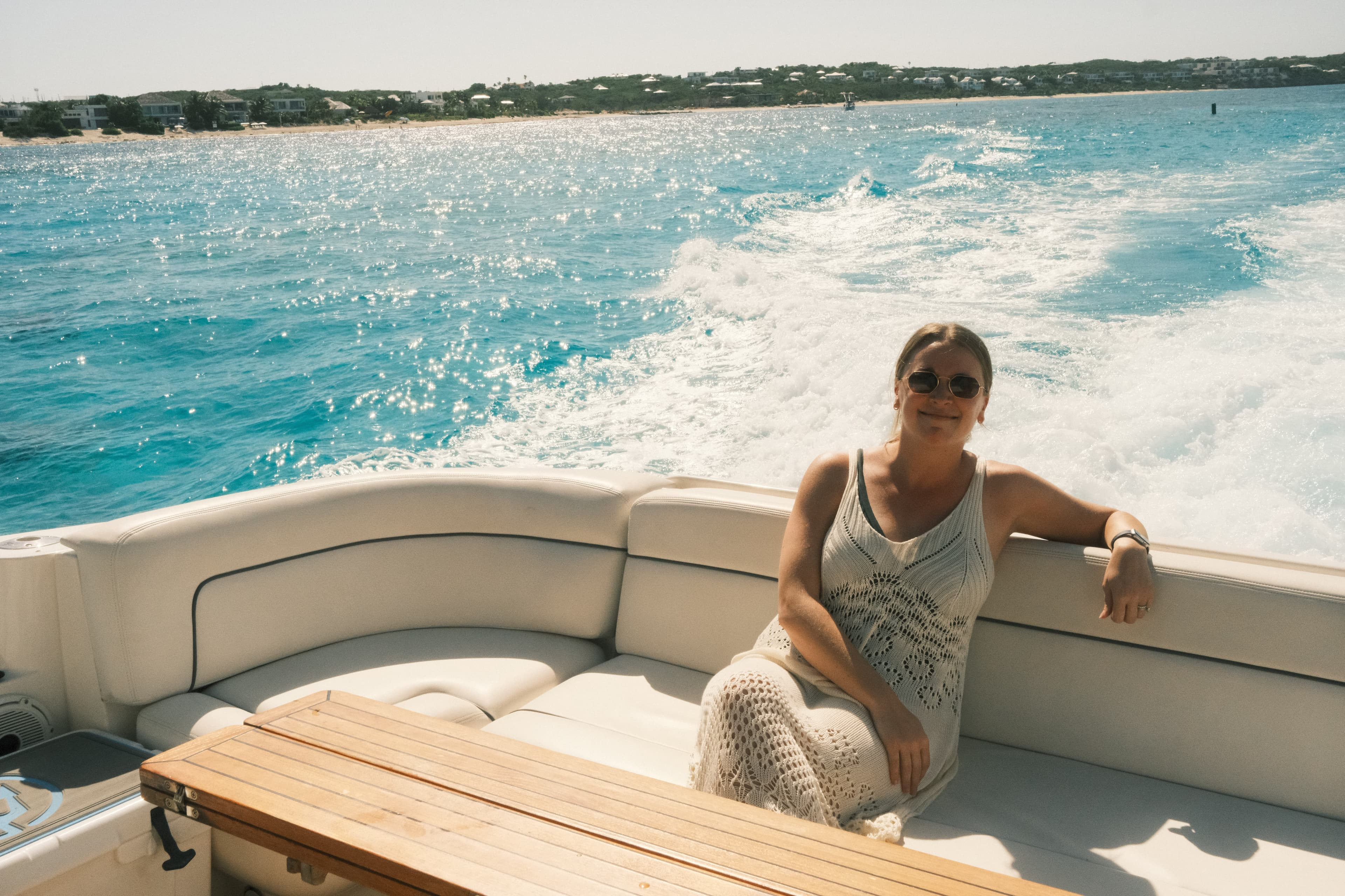 Gloria in a white macrame dress on a bench on a yacht in the ocean