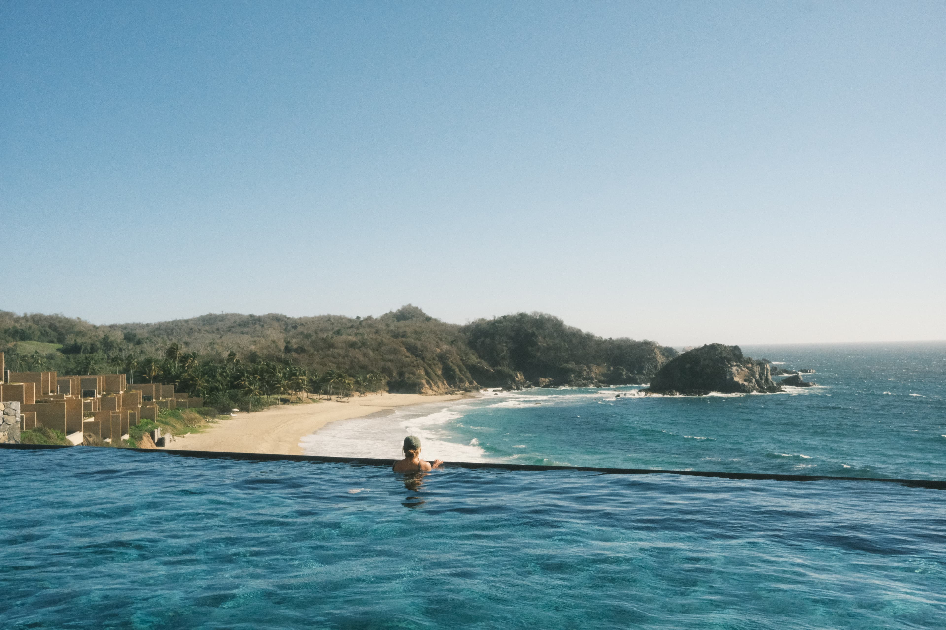 Gloria at the edge of an infinity pool with her back to the camera overlooking the ocean