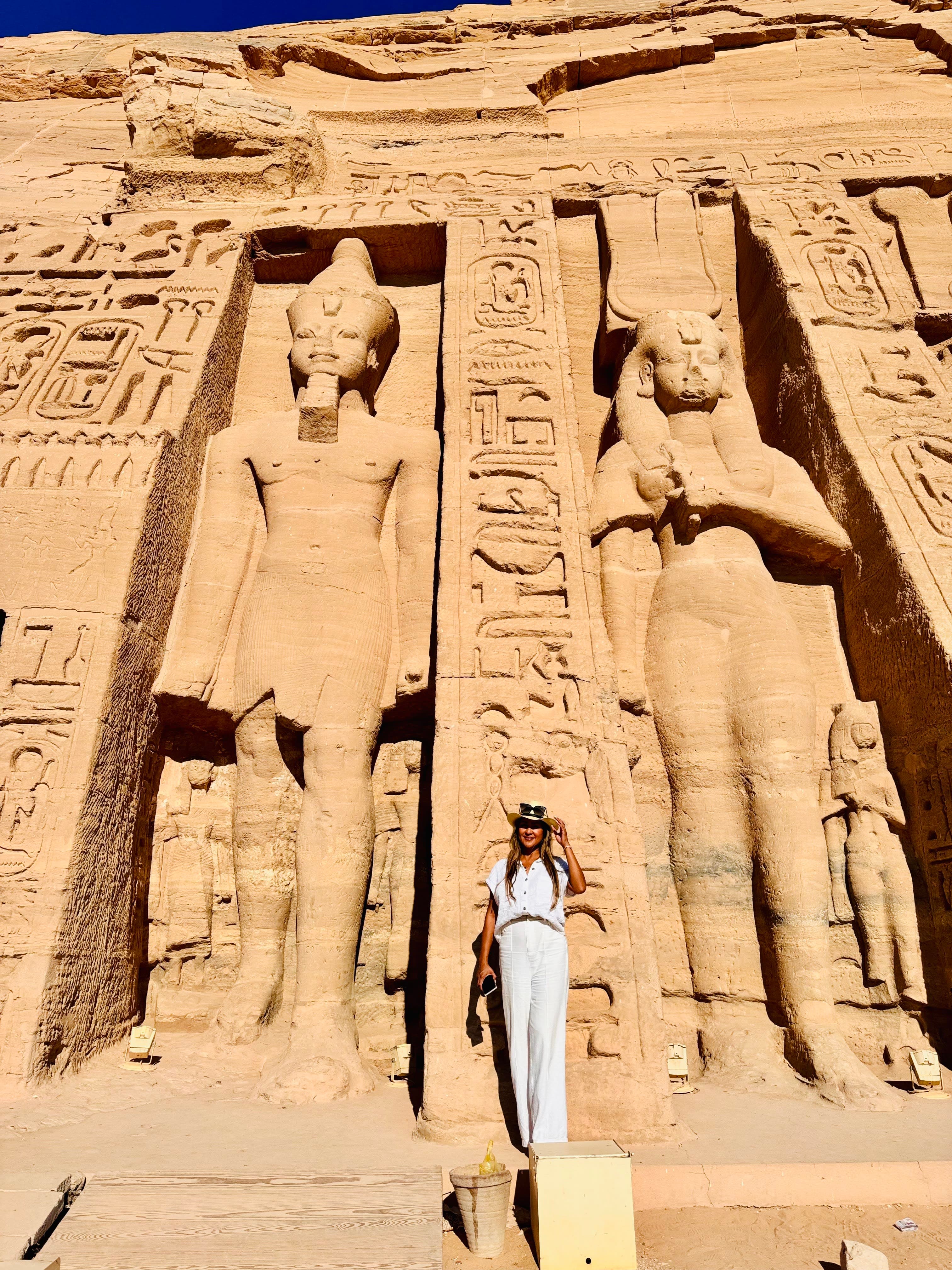 Wendy in a white outfit posing for a photo at Abu Simbel Temples standing next to carved statues